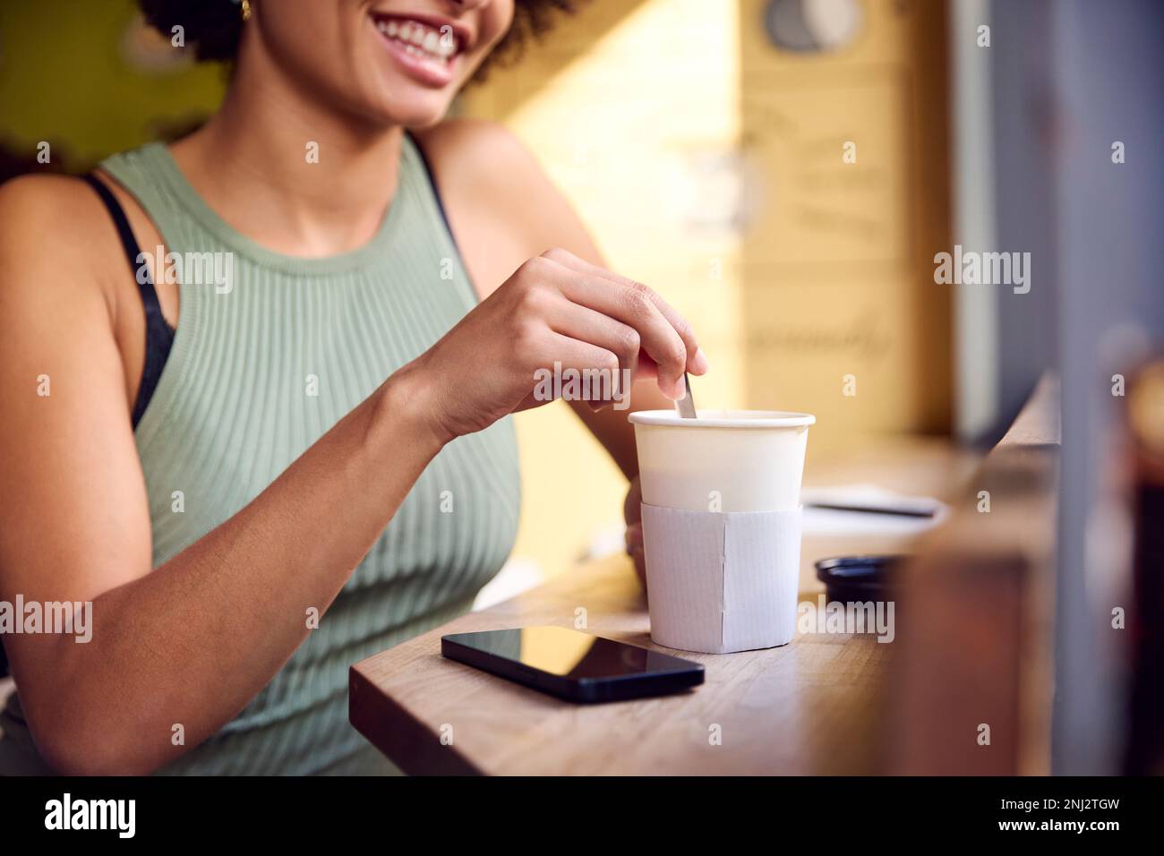 Primo piano del cliente femminile nella finestra del caffè mescolando bevanda calda nella tazza di Takeaway con agitatore di legno Foto Stock