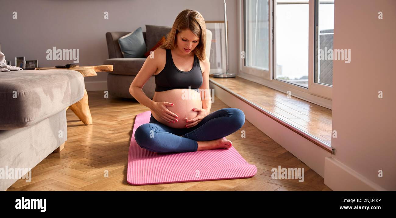 Donna incinta che indossa l'abbigliamento di idoneità sul tappeto di esercitazione a casa che fa lo yoga Foto Stock
