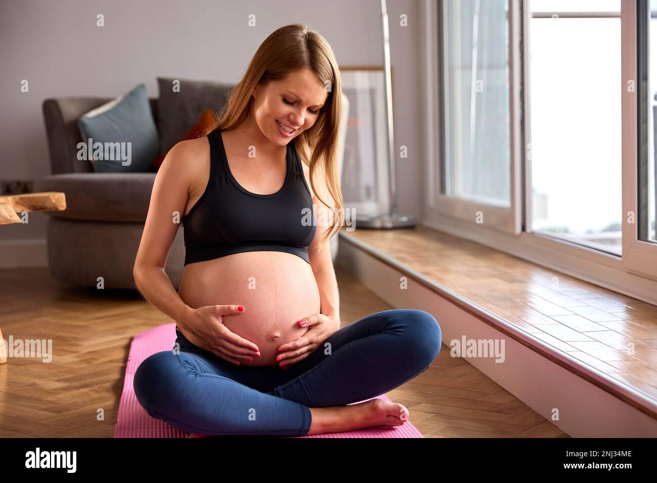 Donna incinta che indossa l'abbigliamento di idoneità sul tappeto di esercitazione a casa che fa lo yoga Foto Stock