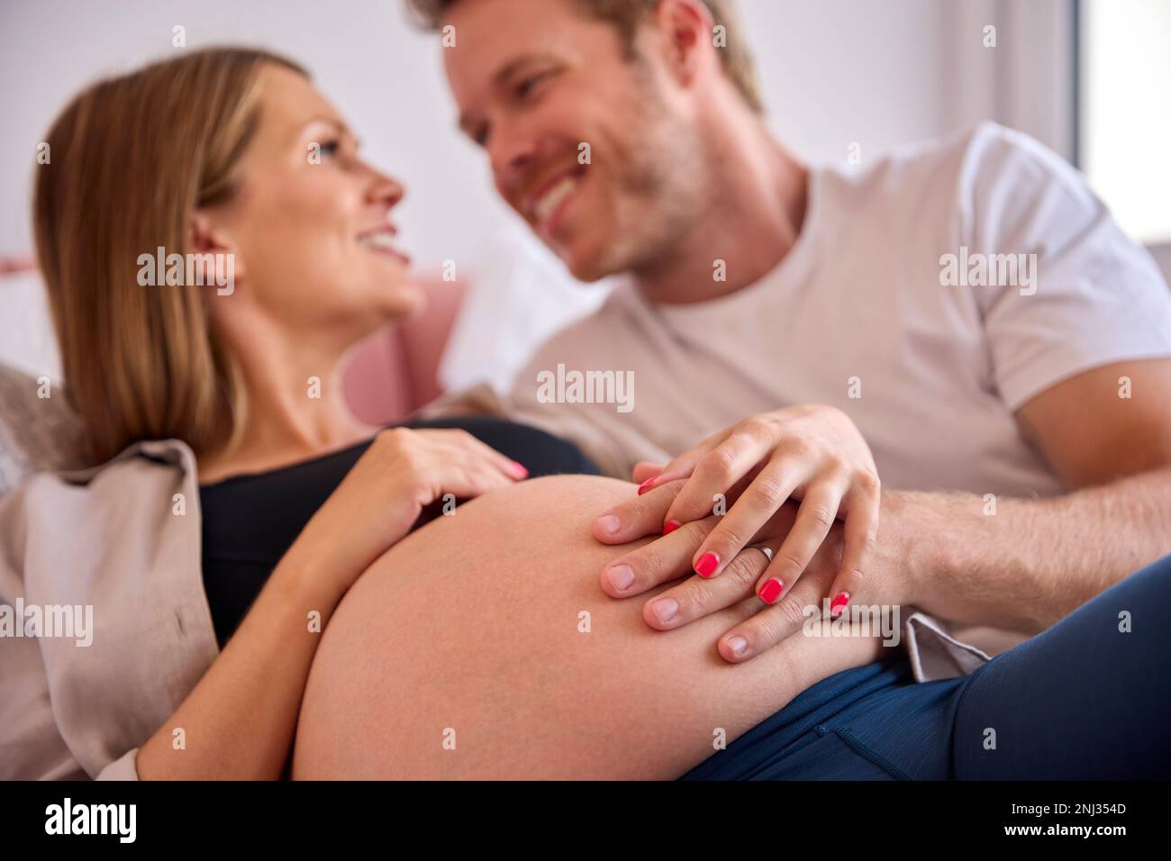 Coppia amorevole a casa sdraiata sul letto con l'uomo che tocca lo stomaco della donna incinta Foto Stock