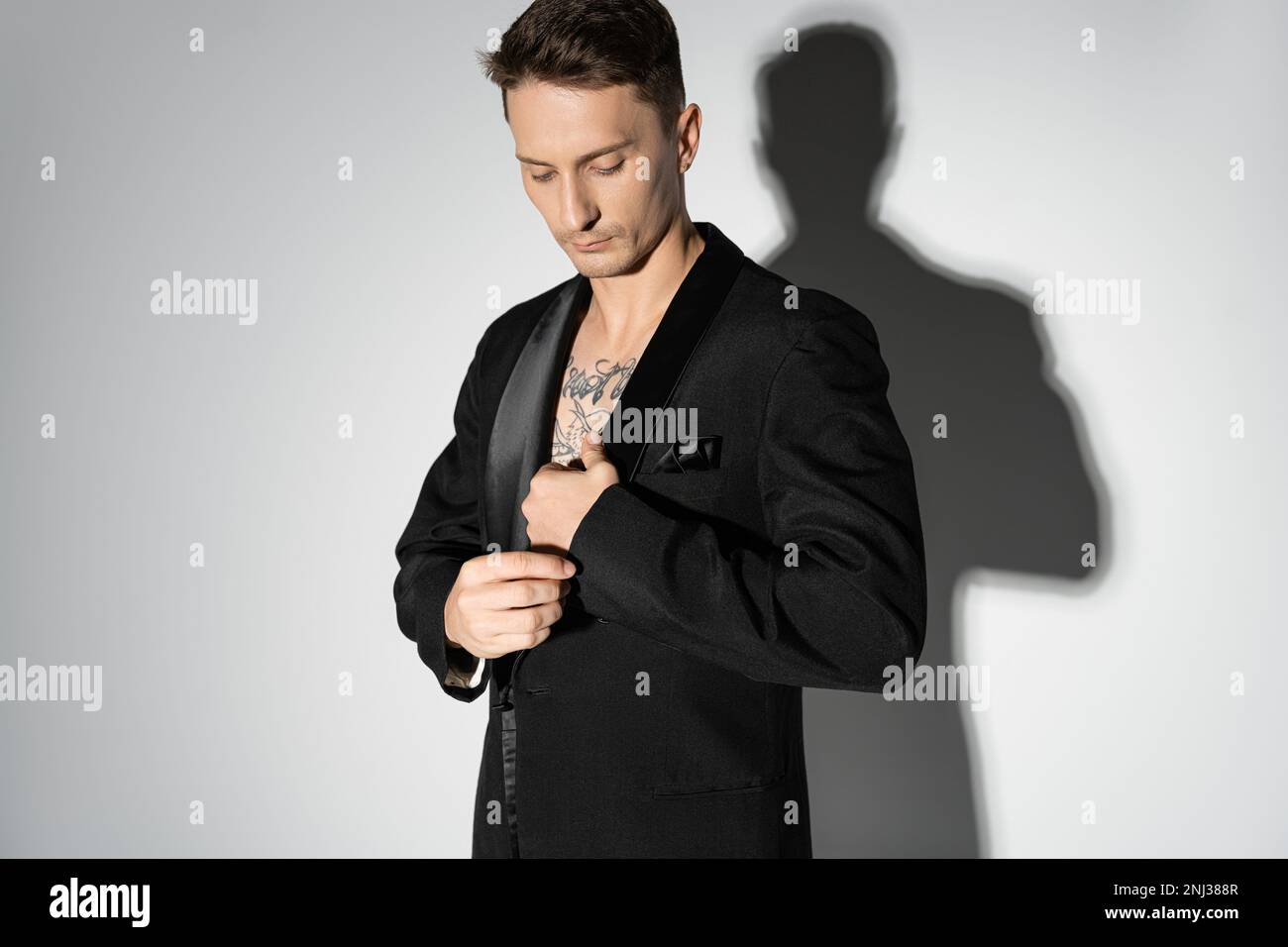 manica di regolazione uomo tatuato di nero elegante blazer su sfondo grigio con ombra, immagine stock Foto Stock