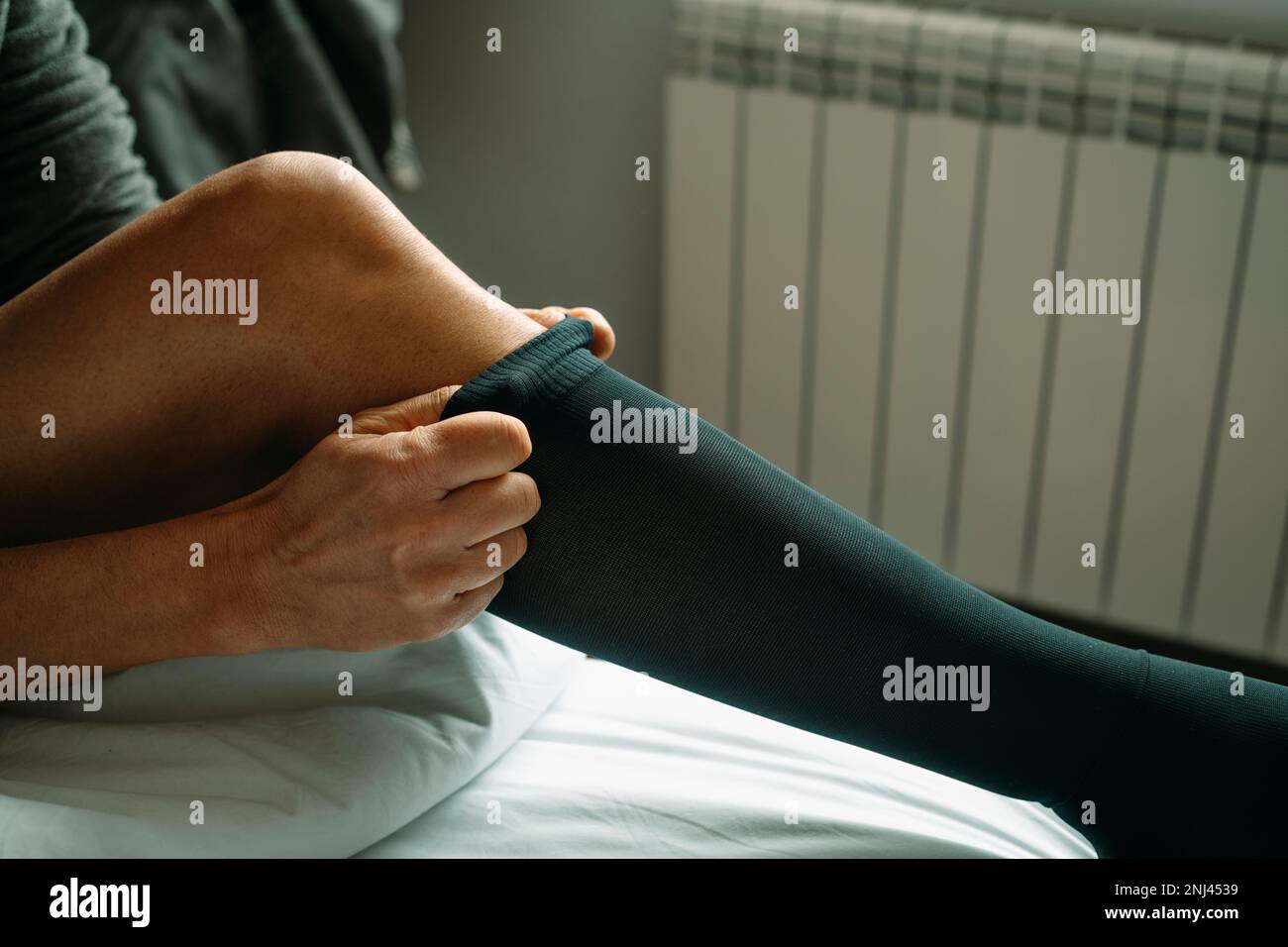 primo piano di un uomo che si mette su una calza a compressione seduta sul letto a casa Foto Stock