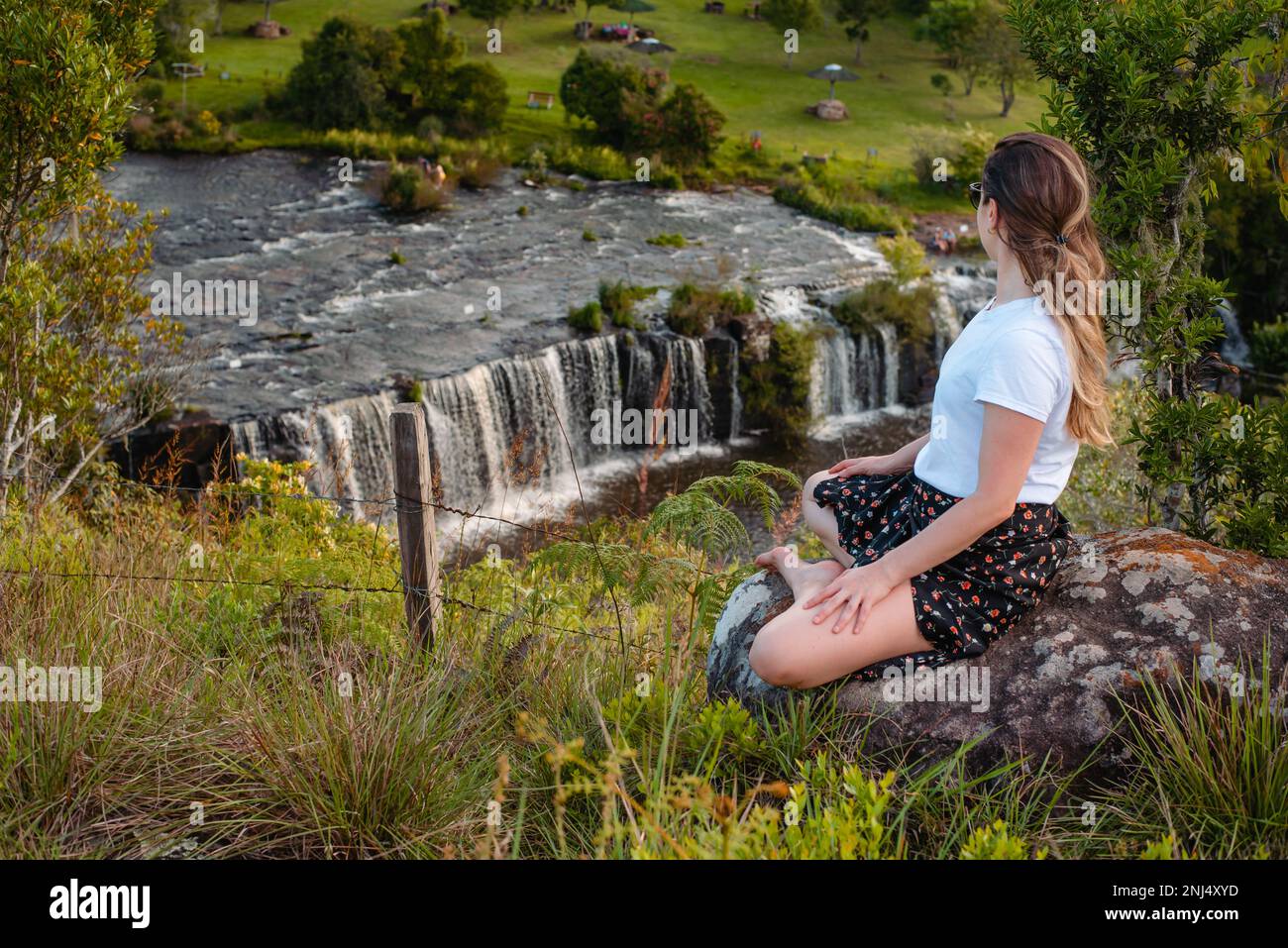 donna seduta croce zampe alle cascate ammirando la vista Foto Stock