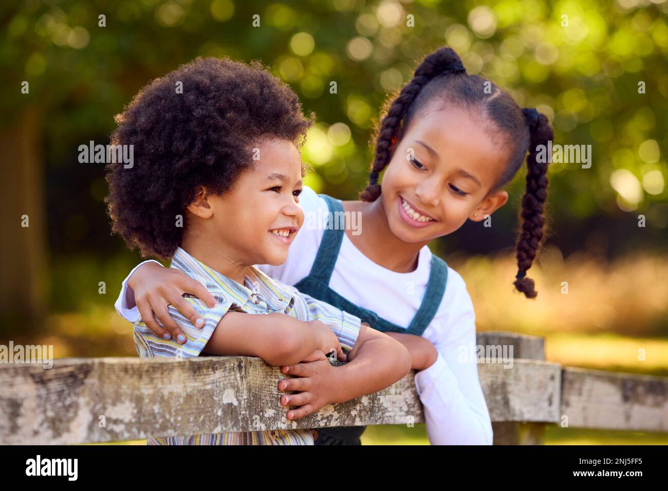 Due bambini sorridenti che si appoggiano a Fence a piedi in campagna Foto Stock