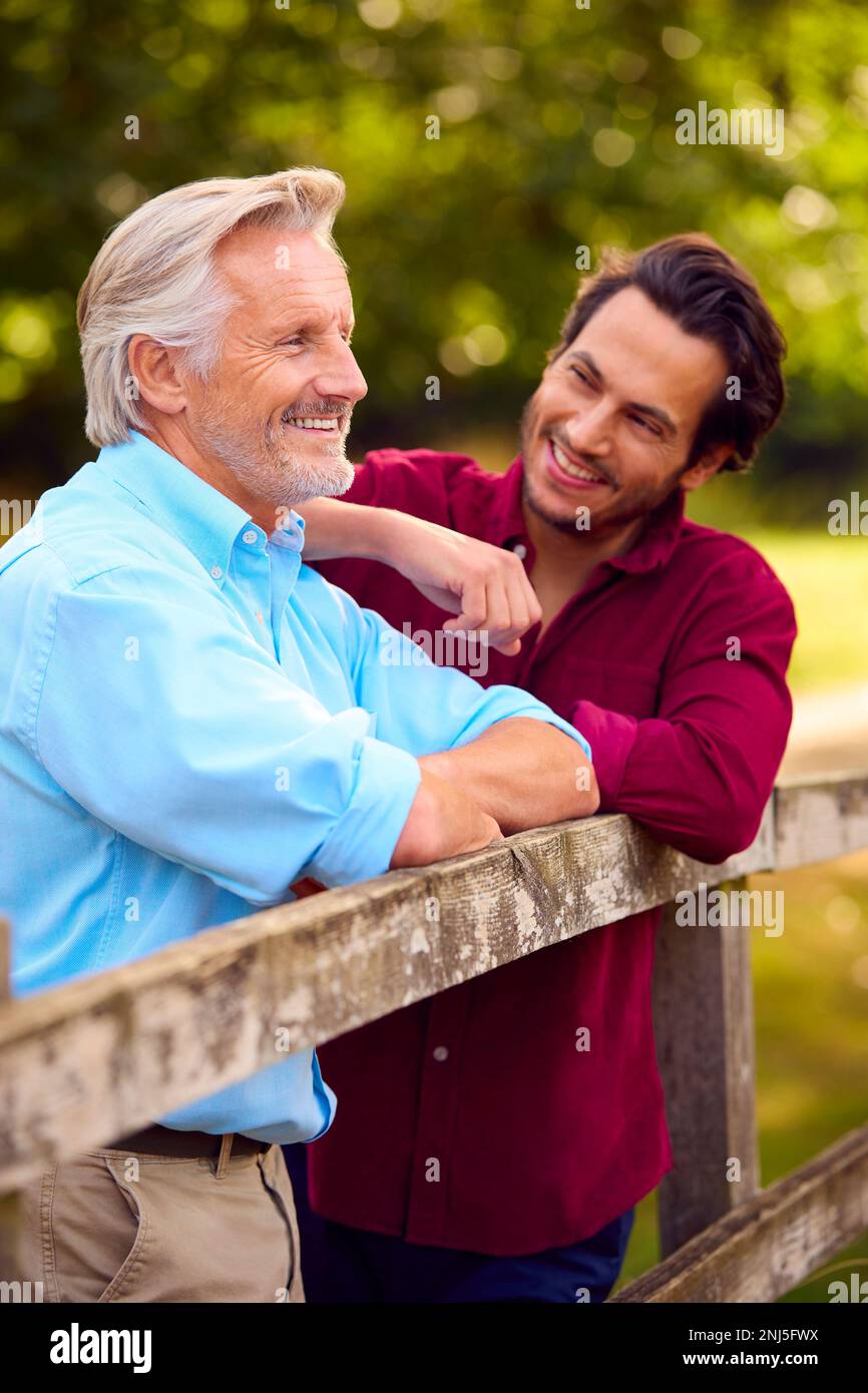 Padre maturo con razza mista Figlio adulto che pende su Fence Walking in campagna Foto Stock