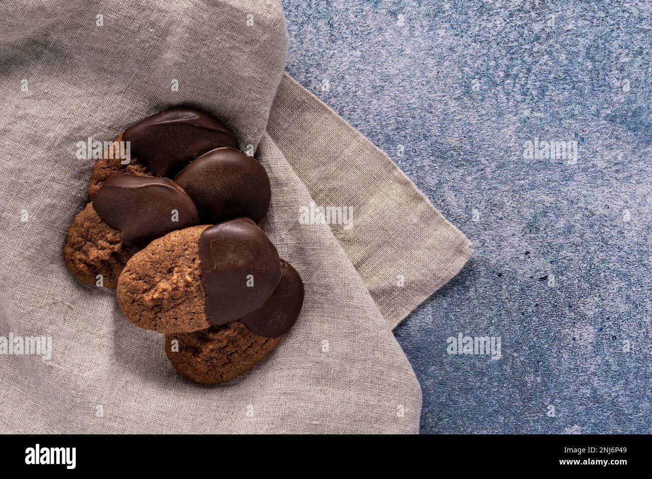 biscotti spritz al cioccolato immersi nel cioccolato che si stendano su un tovagliolo di lino seduto su uno sfondo blu chiazzato Foto Stock