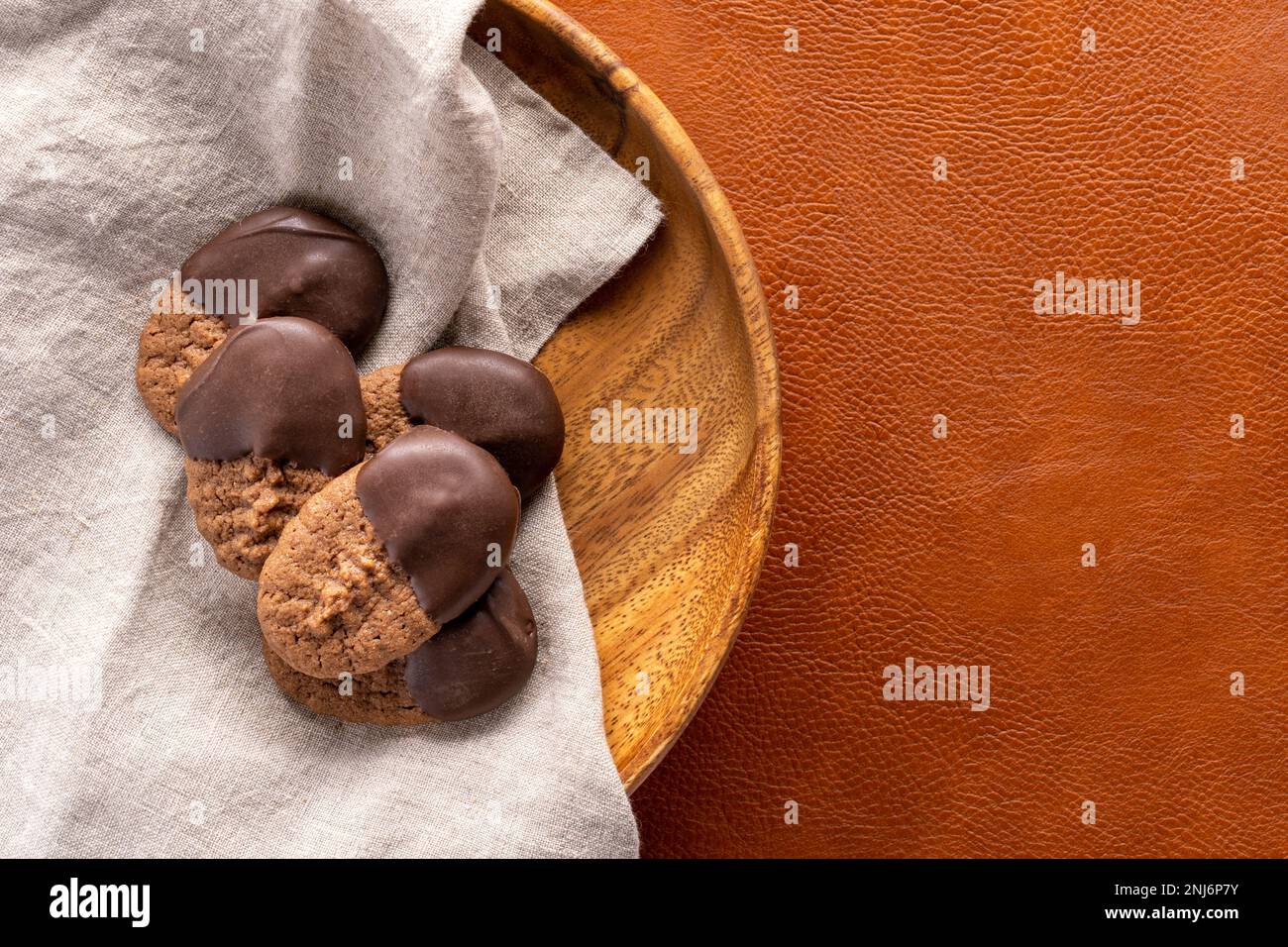 biscotti al cioccolato con spritz immersi nel cioccolato seduti su un piatto di legno con un tovagliolo di lino su uno sfondo di pelle marrone Foto Stock