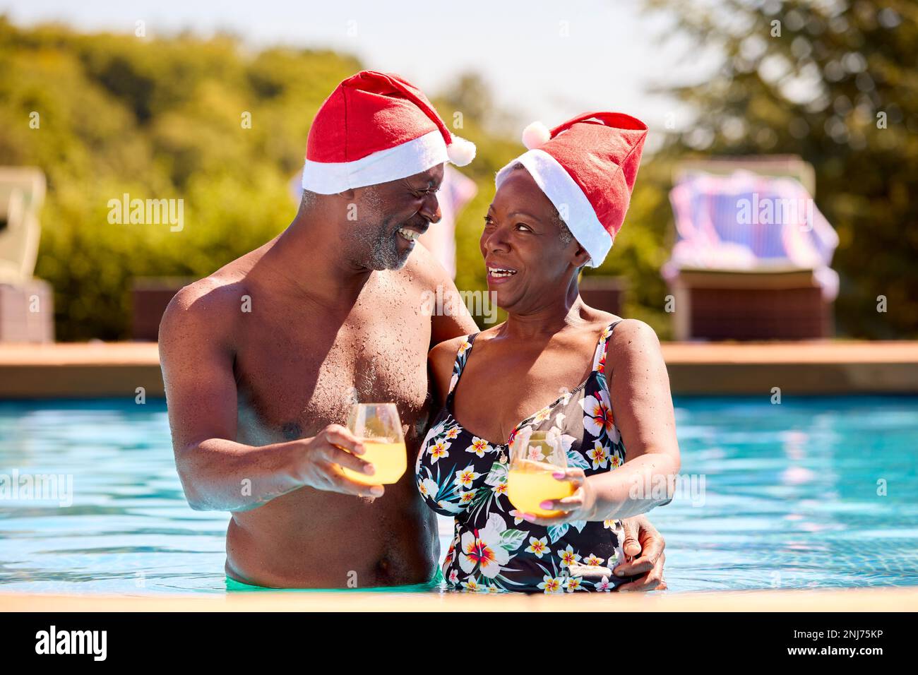 Coppia anziana in vacanza di Natale in piscina con berretti di Santa Foto Stock