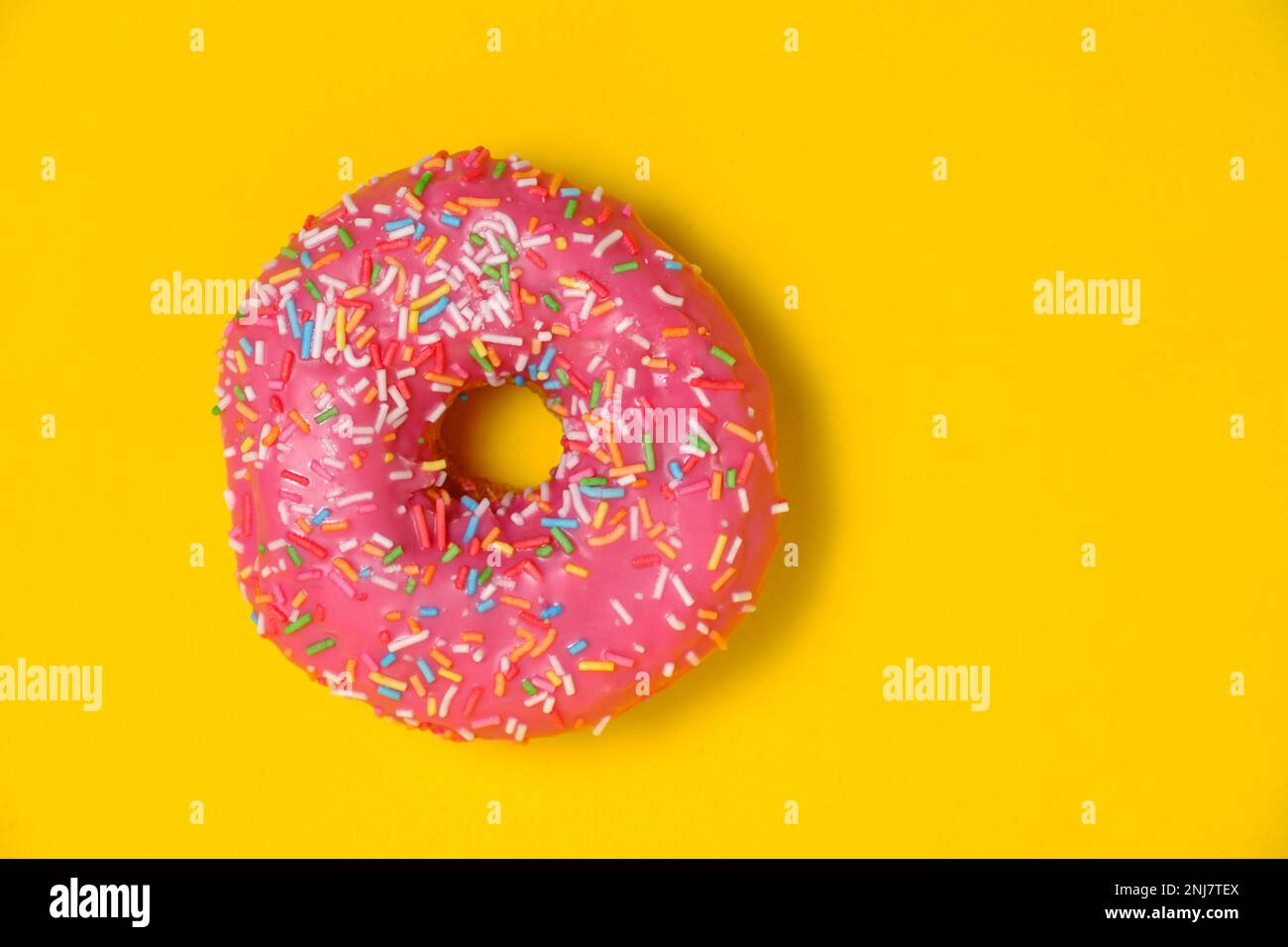 Ciambella con glassa rosa e zuccherini multicolore. Su fondo giallo Foto Stock