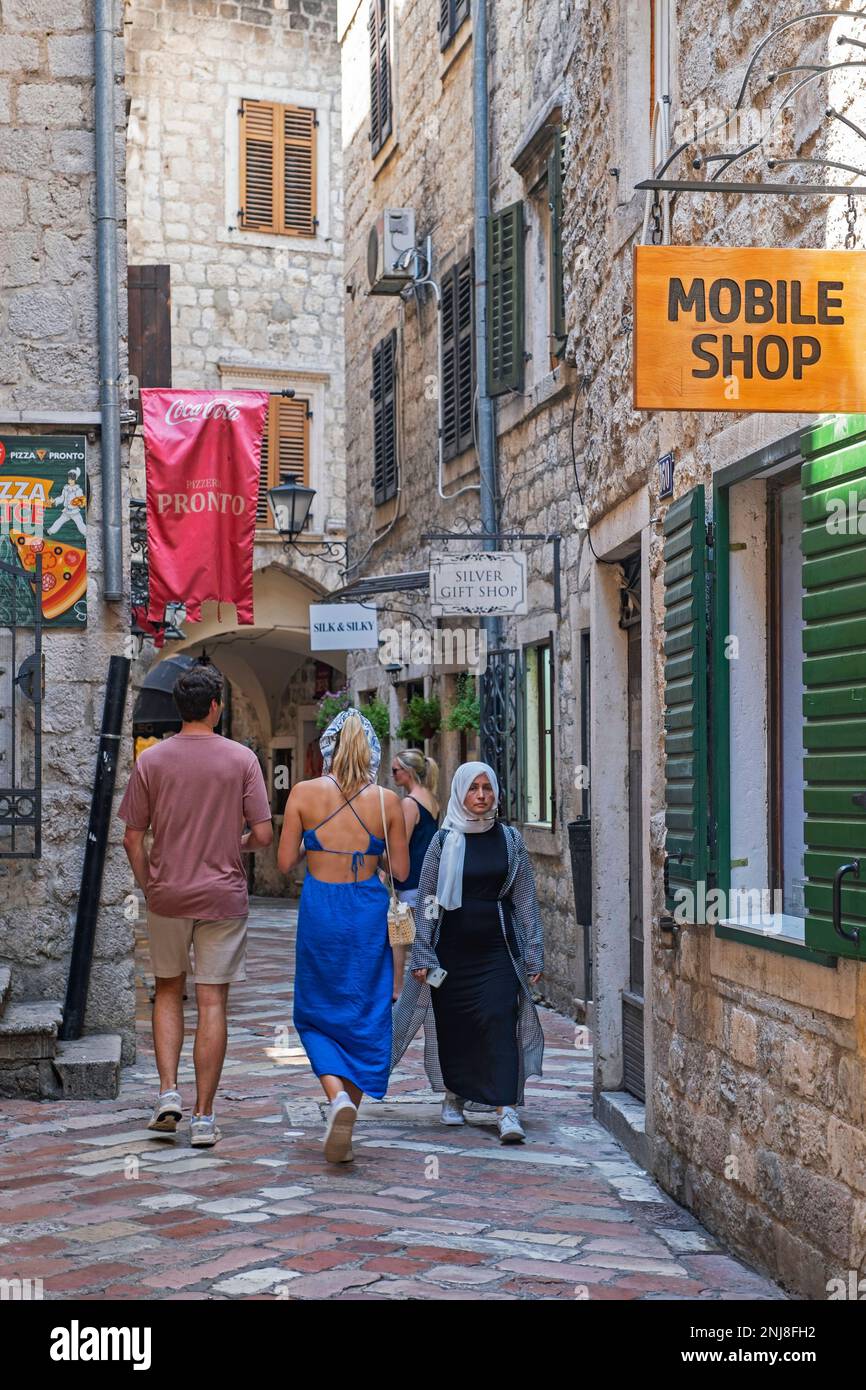 Turisti occidentali e donne musulmane / muscima shopping in vicolo stretto nel centro storico veneziano della città di Cattaro, sud-ovest Montenegro Foto Stock