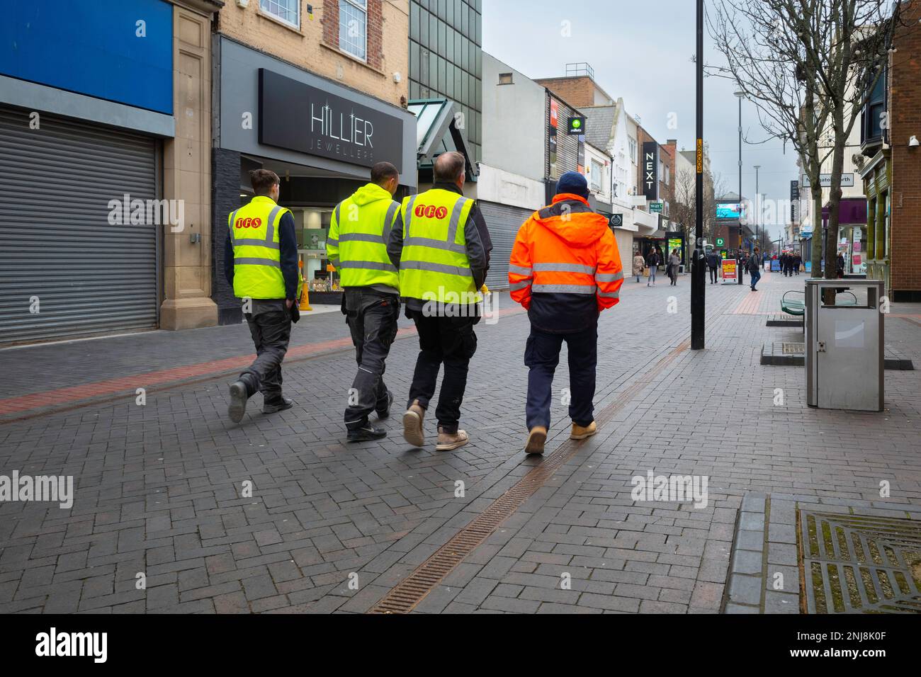 Un gruppo di quattro uomini che lavorano in abbigliamento hi vis camminare abrest su una strada pedonale a Middlesbrough Foto Stock