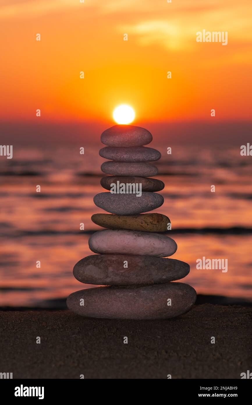 İmage verticale, profilo equilibrato piramidale di ciottoli sulla spiaggia al tramonto. Mare sullo sfondo. Pietre Zen sulla spiaggia di mare, meditazione, spa. Foto Stock
