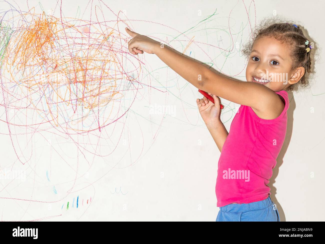 Piccola ragazza brasiliana che scarabocchio, dipinge e disegna su una parete di colore giallo chiaro Foto Stock