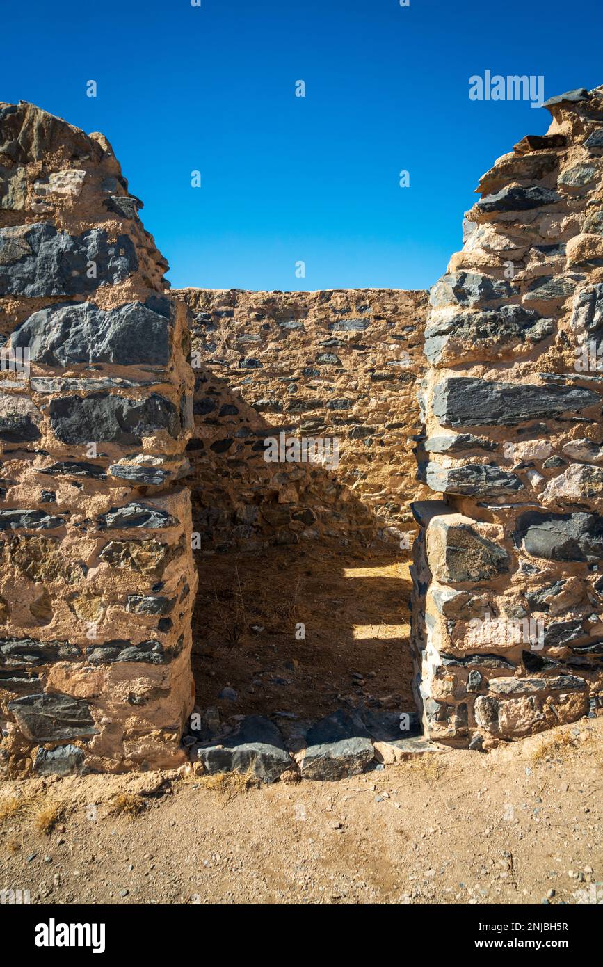Una fessura tra due spesse mura in pietra scura si apre verso un muro interno in ombra e un cielo blu profondo al Fort Bowie National Historic Site, Arizona. Foto Stock