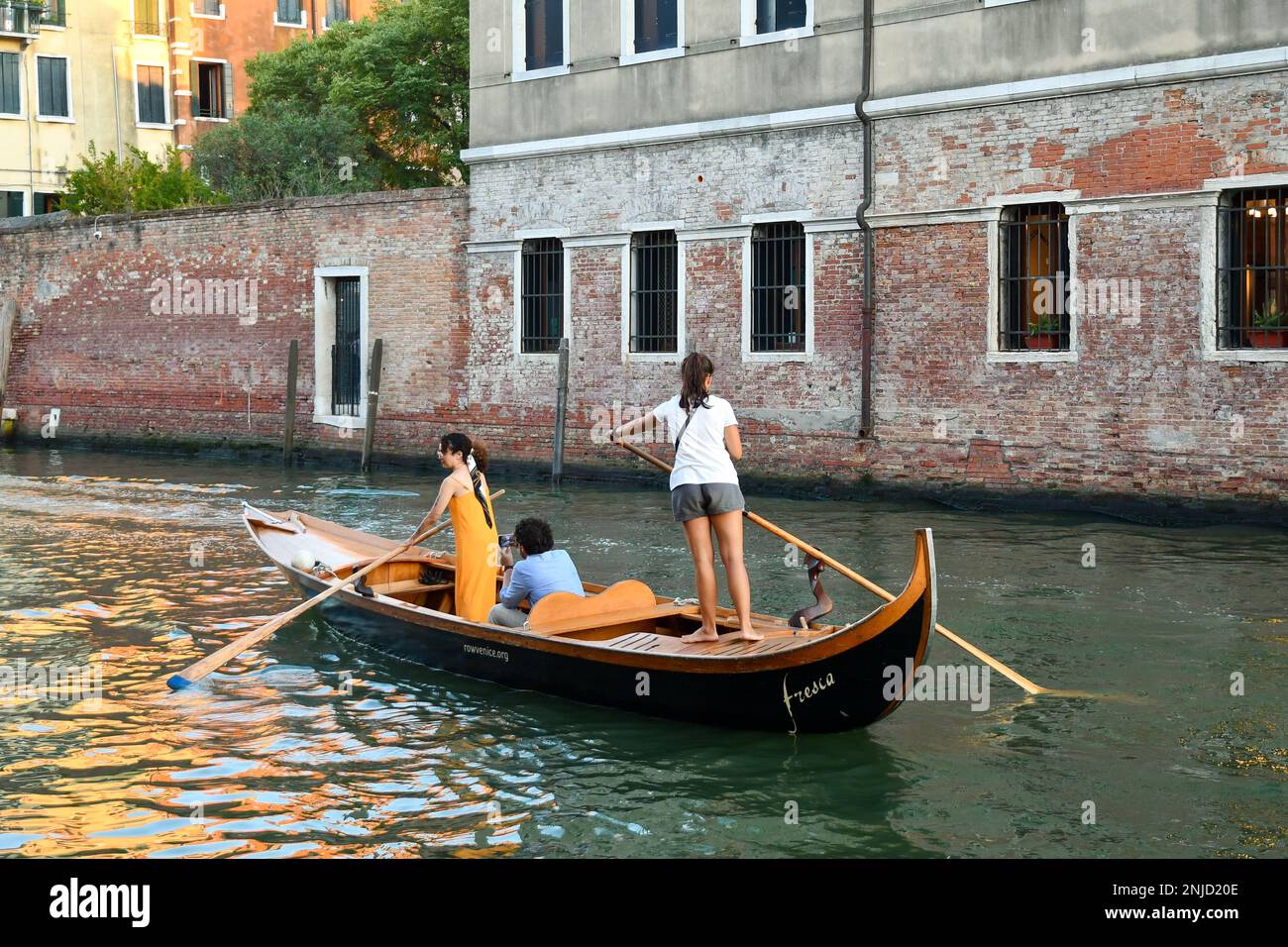 Un paio di giovani donne in piedi canottaggio in stile veneziano sul canale del Rio della Misericordia al tramonto, sestiere di Cannaregio, Venezia, Italia Foto Stock