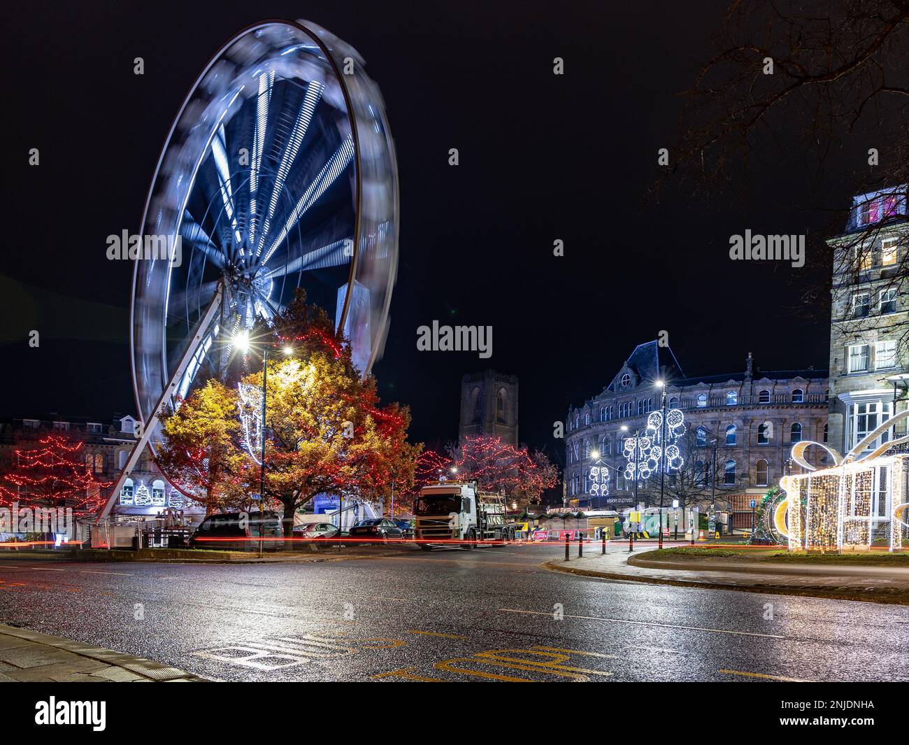 Una ruota panoramica luminosa gira nel centro di Harrogate, circondata da luci natalizie e decorazioni natalizie durante la stagione invernale Foto Stock