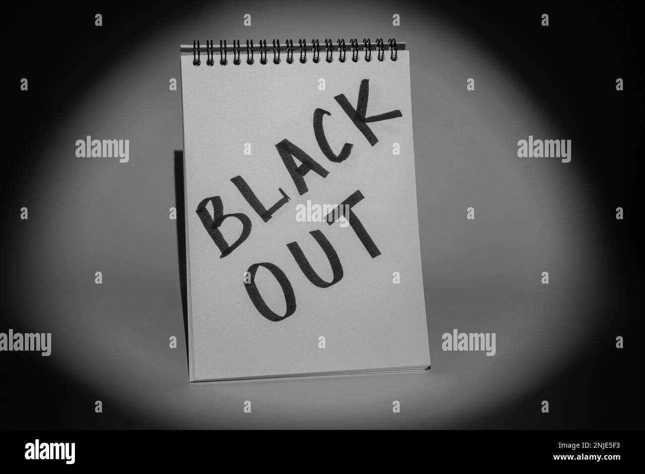 Blocco note con l'iscrizione 'Blackout' su sfondo grigio, illuminato da un riflettore. Immagine monocromatica. Concetto di interruzione dell'alimentazione Foto Stock