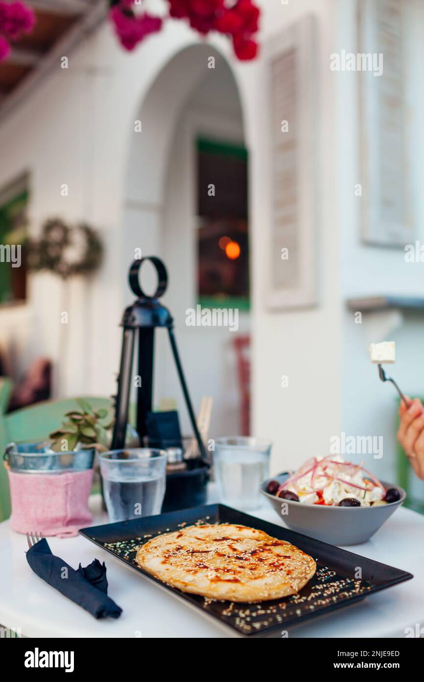 Pita greca morbida, farcita con formaggio cosparso di semi di sesamo, miele, servita con insalata greca e acqua nel caffè all'aperto Foto Stock