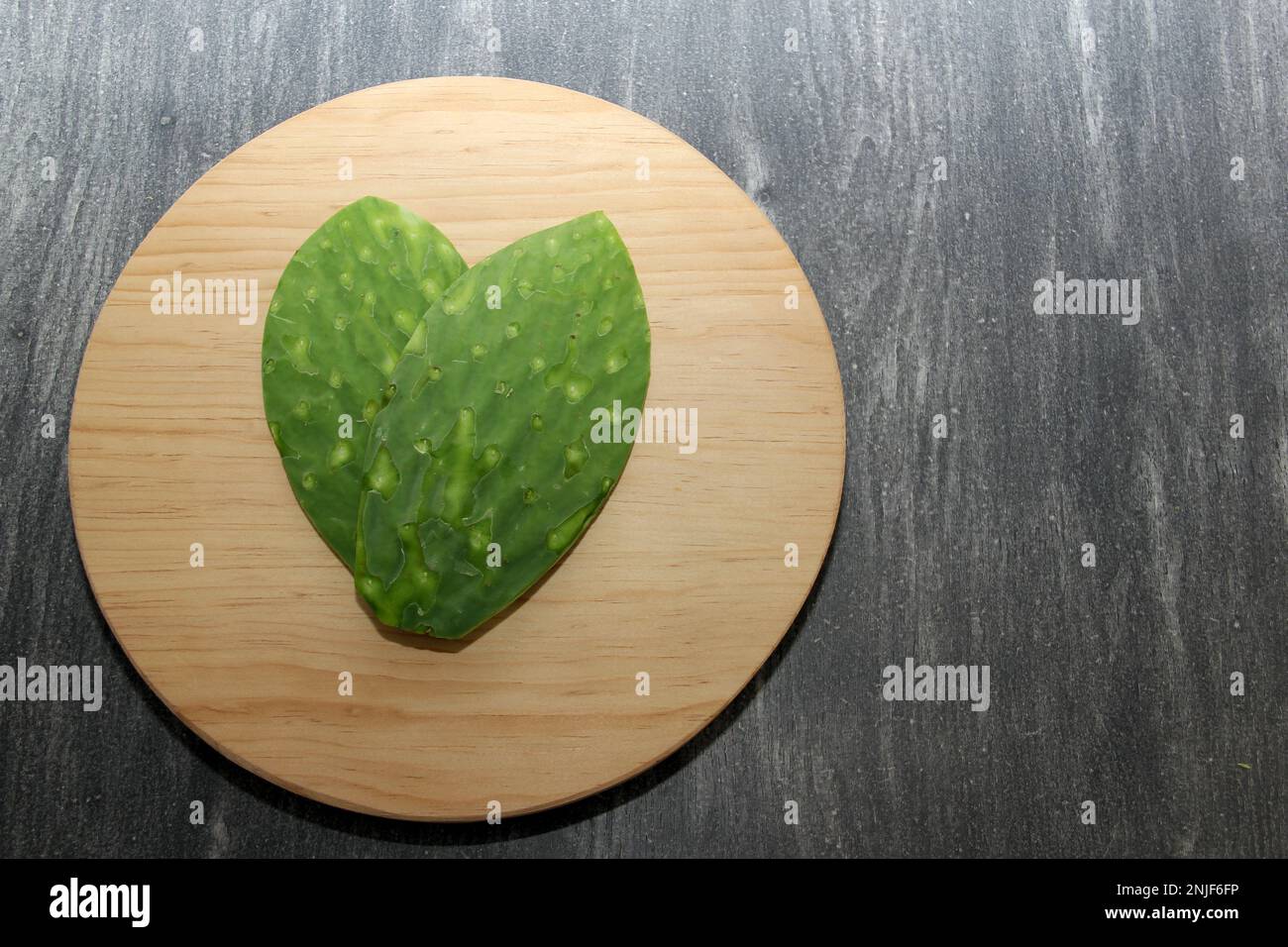 Nopale verde fresco senza ossa su un tagliere di legno rotondo pronto per essere cucinato Foto Stock