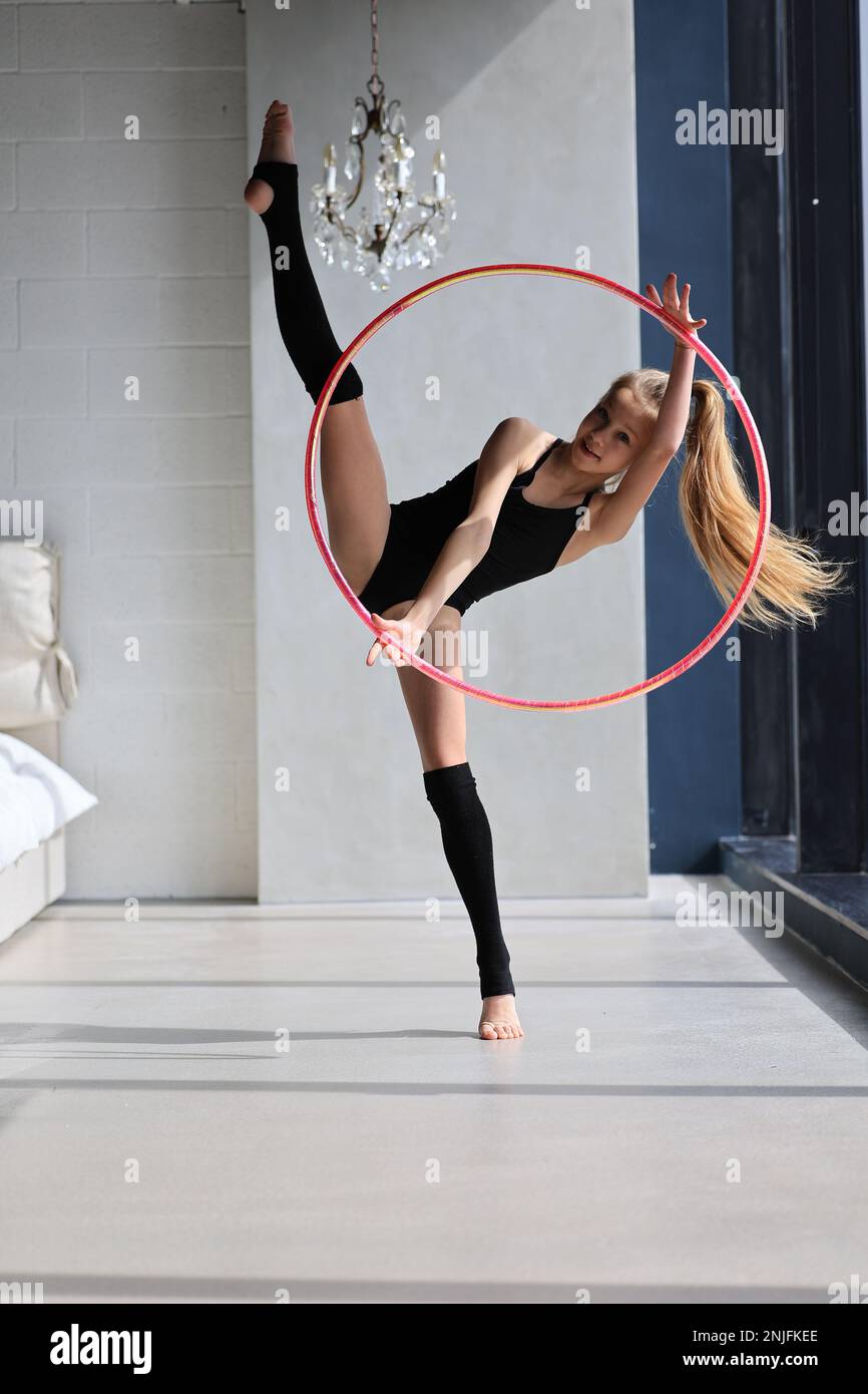 la ragazza piccola ginnastica in vestito nero si esercita con un anello ginnico Foto Stock