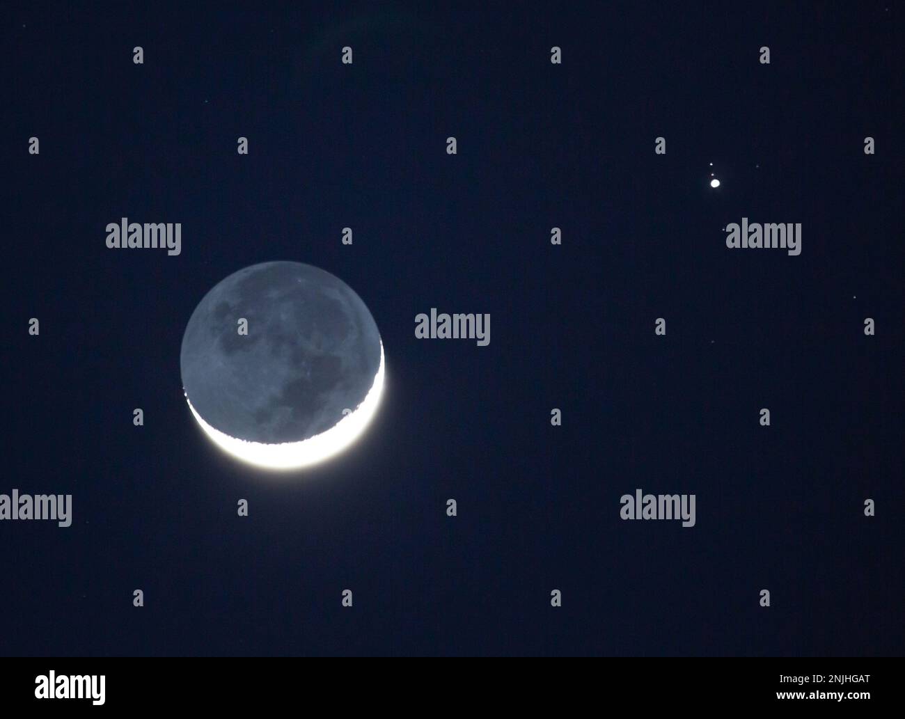 La sera del 22 febbraio 2023 convergono una luna dibbosa cerante e il pianeta Giove. Tre lune galileiane di Giove sono visibili. Foto Stock