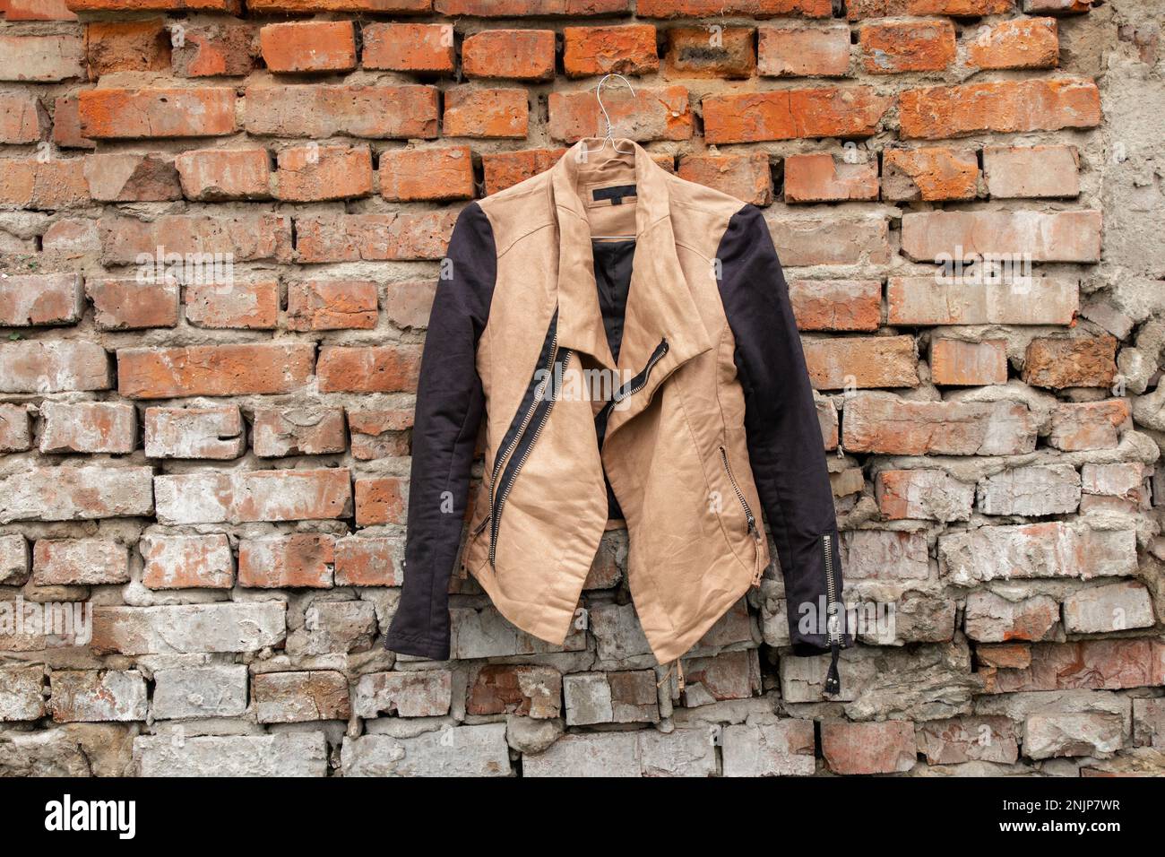 giacca donna marrone appesa su grucce su un vecchio muro di mattoni a casa sulla strada, moda donna Foto Stock