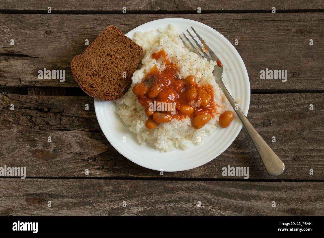 piatto bianco con riso bollito e fagioli con pane su un vecchio asse di legno Foto Stock