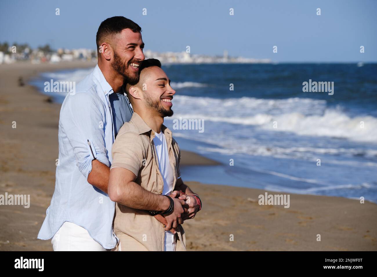 Bella coppia gay sorridente mentre si rilassa sulla spiaggia insieme. Foto Stock