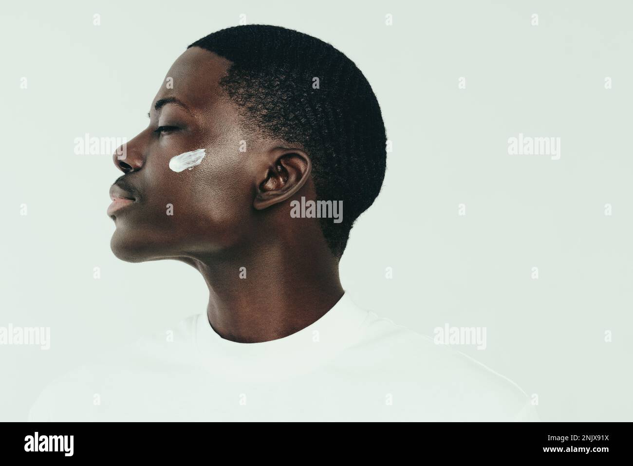 Uomo nero con giovane pelle di melanina applicando una crema idratante sul viso, per mantenere la pelle morbida e liscia. Bel giovane uomo che mantiene la sua n Foto Stock