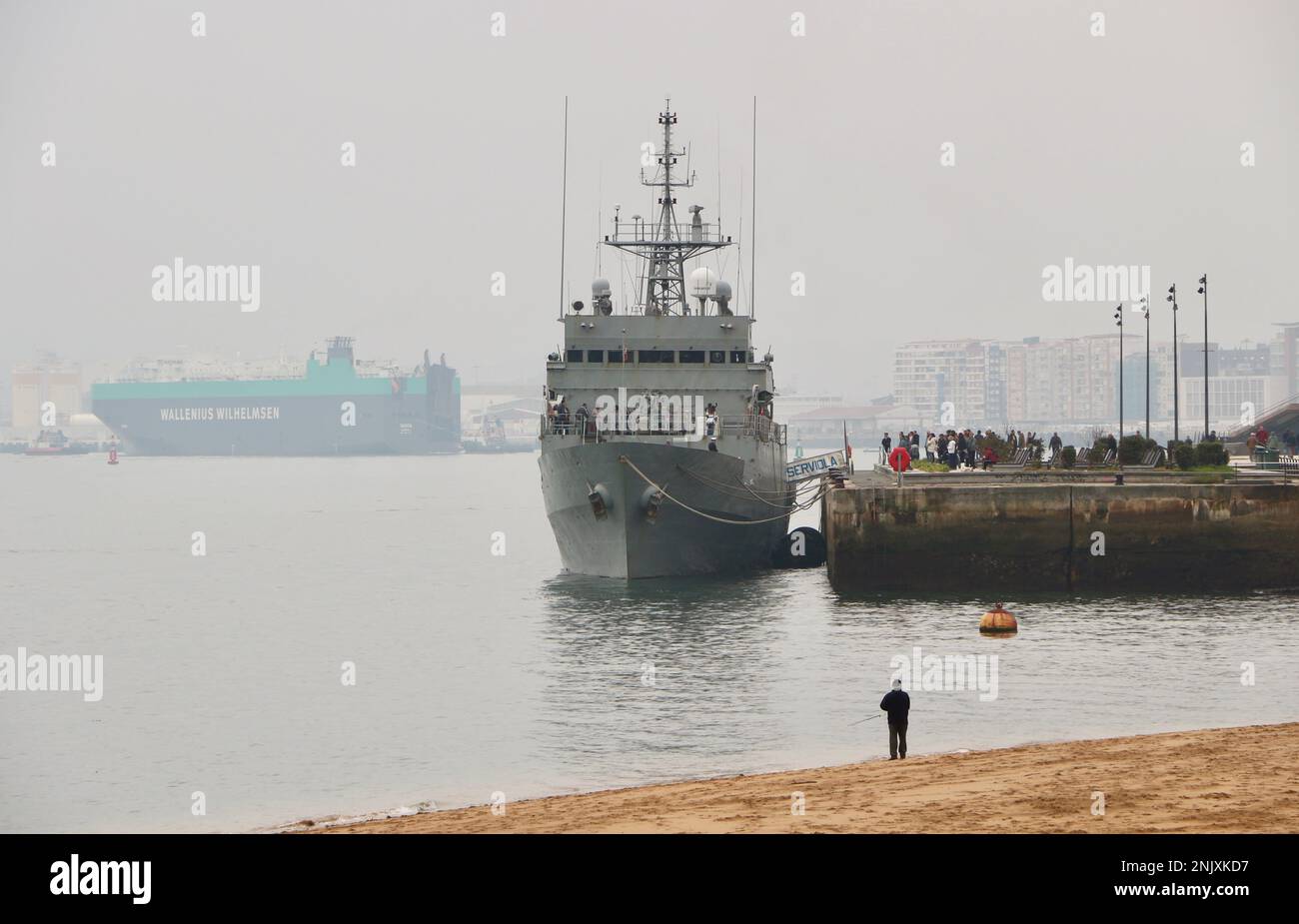 Uomo che pesca sulla spiaggia con la pattuglia spagnola Serviola P-71 aperto al pubblico ormeggiato nella zona del porto di Gamazo di Santander Bay Cantabria Spagna Foto Stock