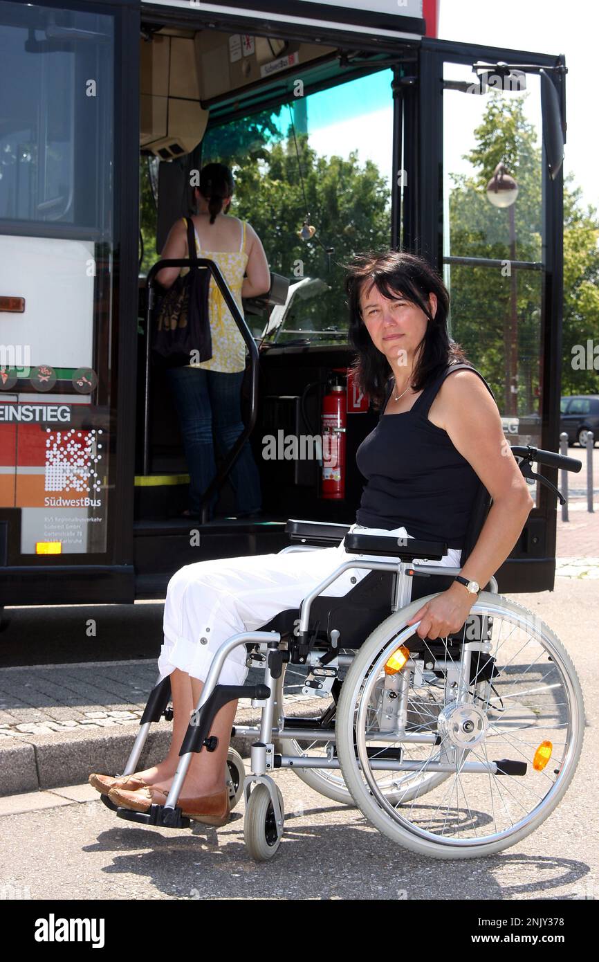 donna su una sedia a rotelle di fronte a una porta dell'autobus aperta Foto Stock