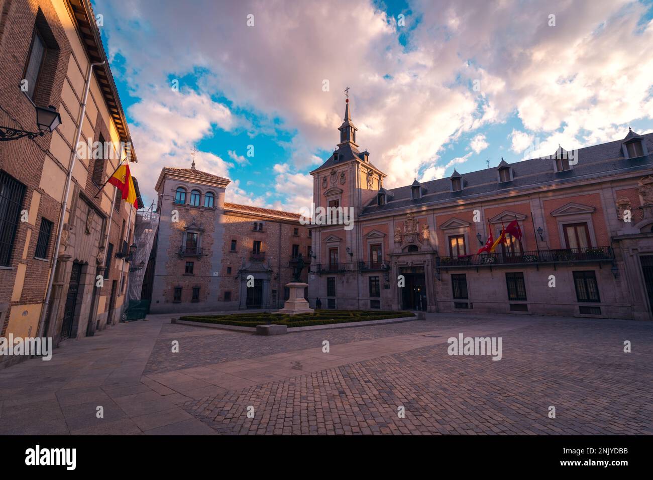 Facciata della cattedrale con croce in cima vicino all'edificio contro il cielo blu nuvoloso sulla piazza di Madrid Foto Stock