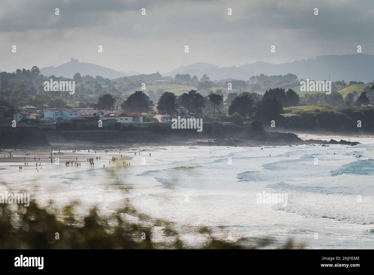 Scenario mozzafiato di oceano panoramico con onde schiumose spiaggia di sabbia vicino a case residenziali e lussureggianti alberi verdi che crescono sulle colline al tramonto in Un Foto Stock