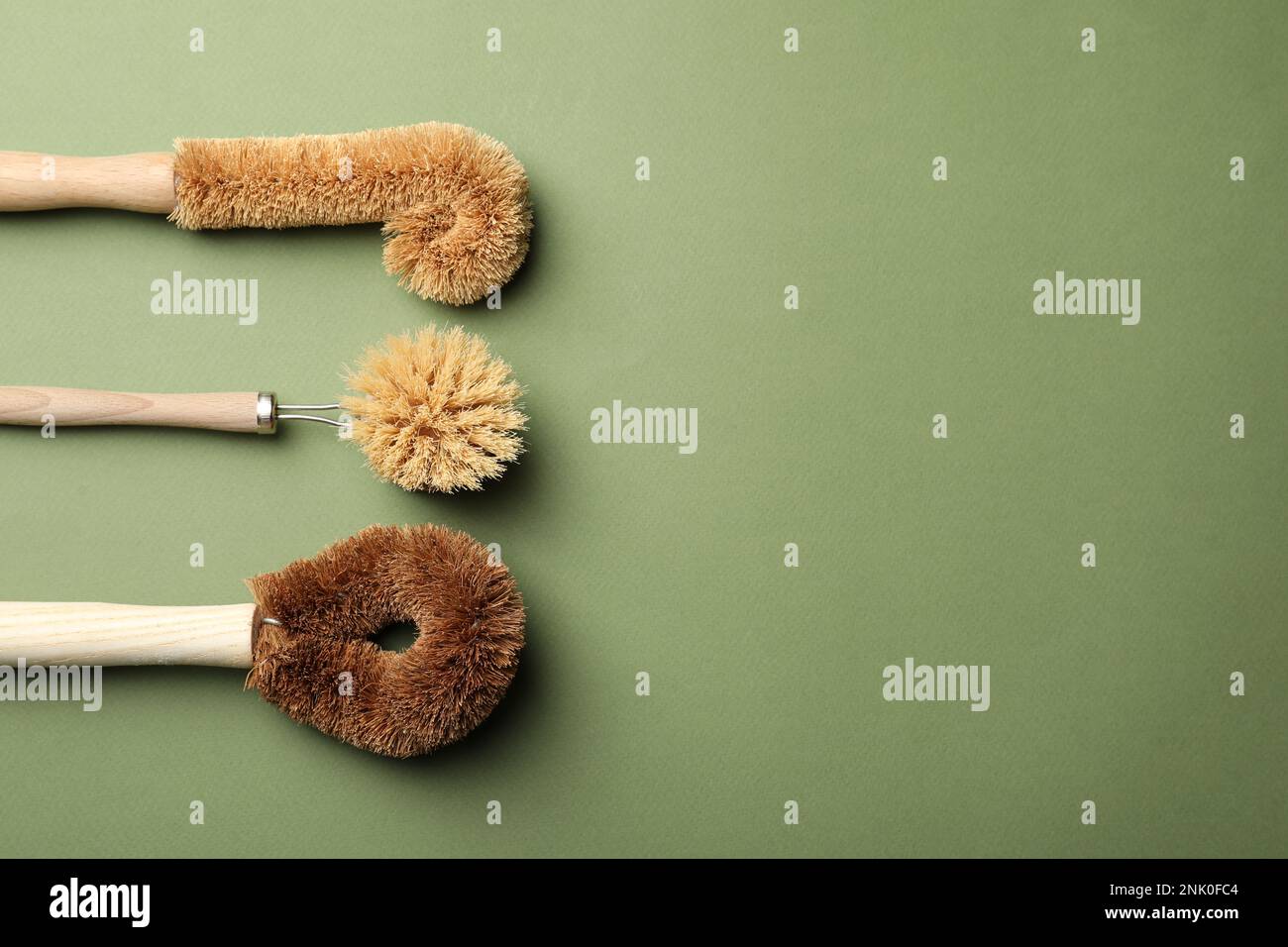 Spazzole di bambù diverse per il lavaggio dei piatti su fondo verde, piatto. Consumo consapevole Foto Stock