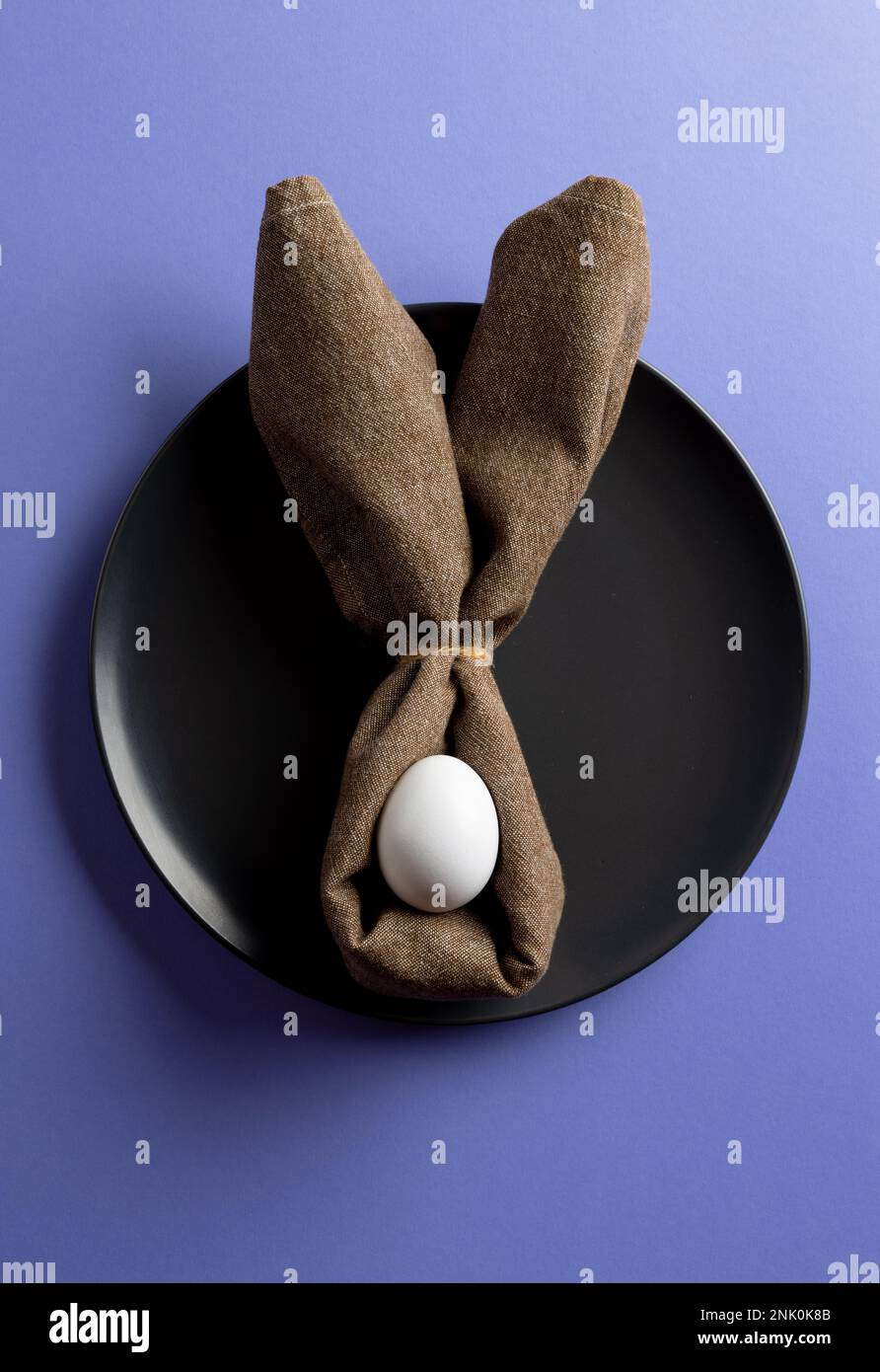 Immagine dell'uovo bianco di pasqua e delle orecchie conigliate sul piatto nero e spazio copia su sfondo viola Foto Stock