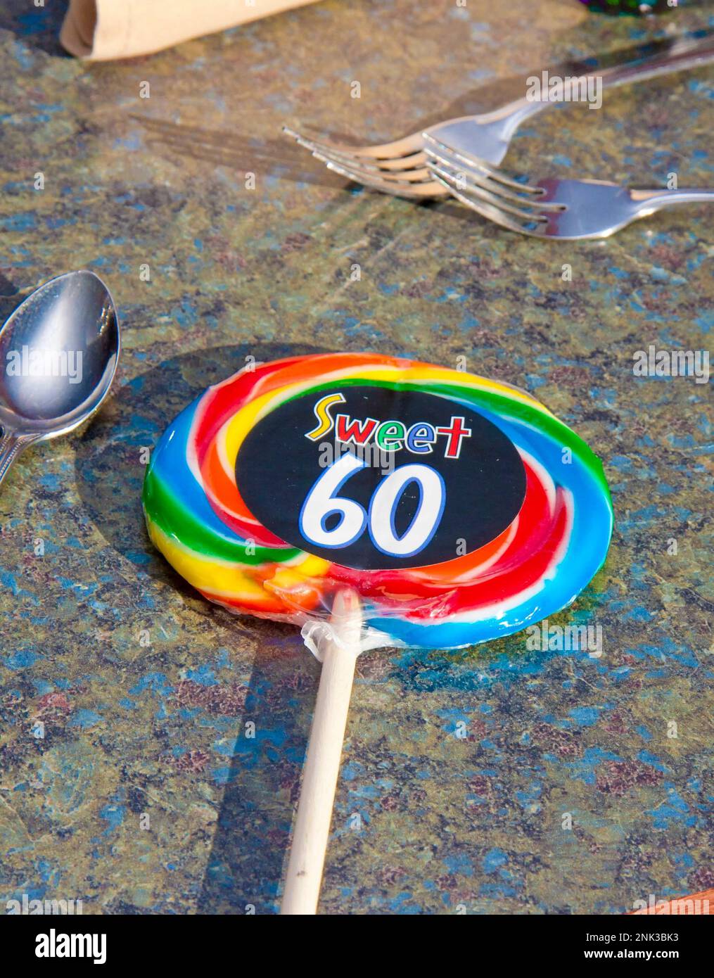 Un grande lollipop colorato si posa sul tavolo del partito con un adesivo Sweet 60 per la ragazza di compleanno che ha girato sessant'anni Foto Stock