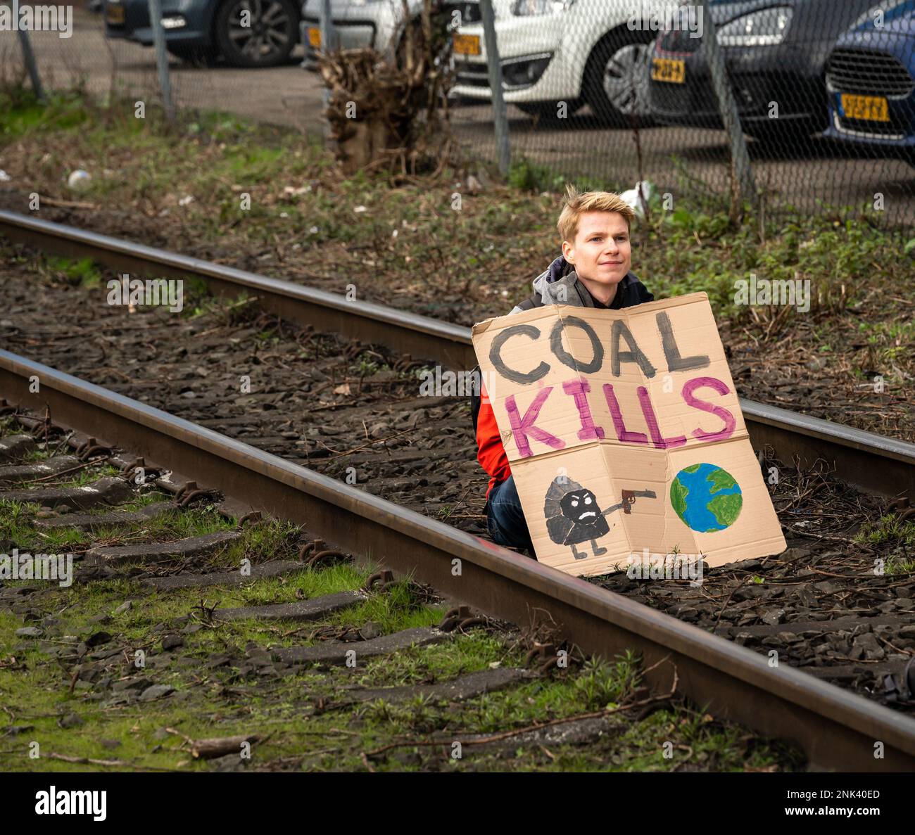 Amsterdam, Paesi Bassi, 22.03.2023, giovane attivista del clima seduto su una rotaia utilizzata per il trasporto del carbone con un cartello che dice "il carbone uccide" Foto Stock