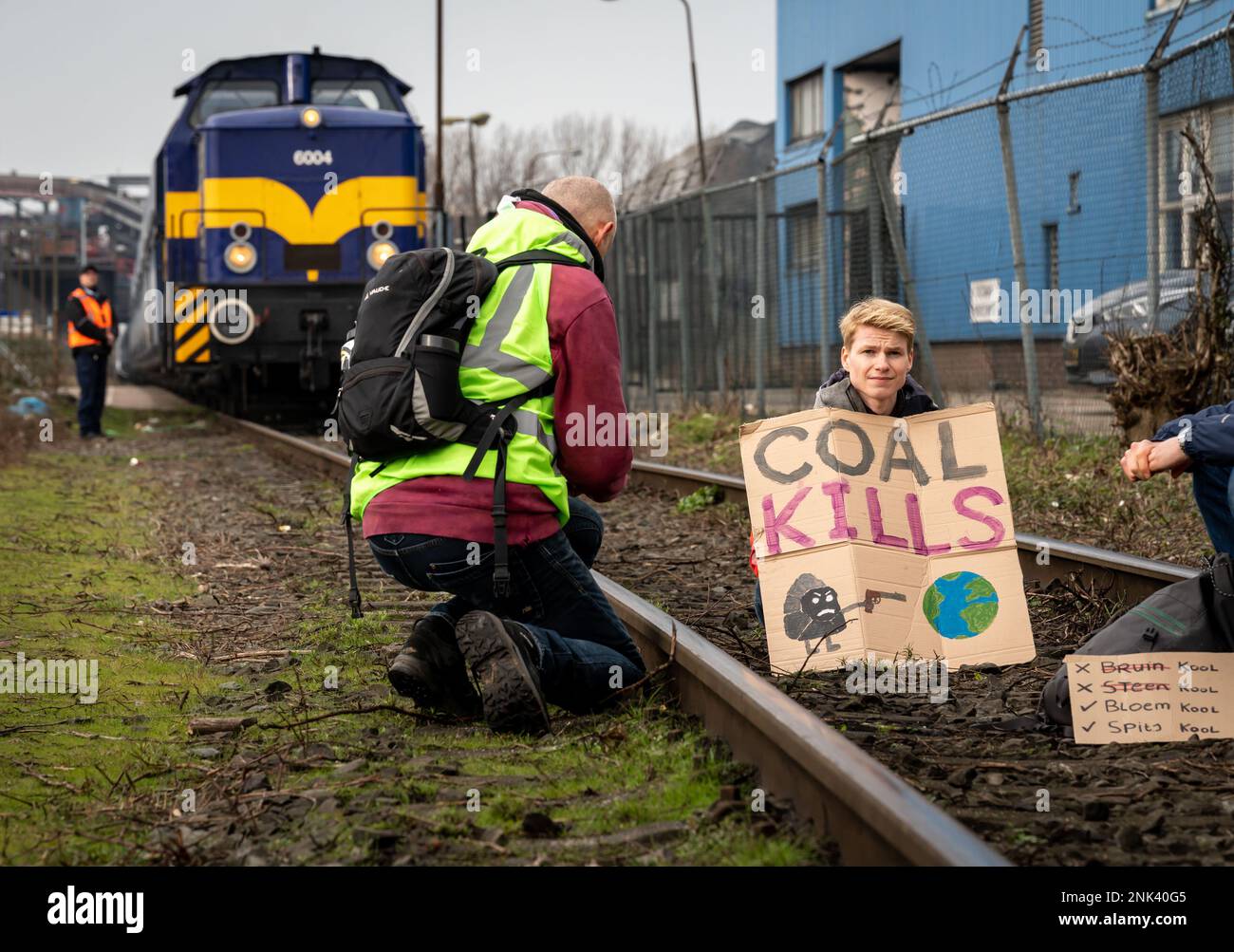 Amsterdam, Paesi Bassi, 22.03.2023, attivista del clima seduto su una rotaia utilizzata per il trasporto del carbone con un cartello con la scritta "Coal Kills" (uccisioni del carbone) Foto Stock
