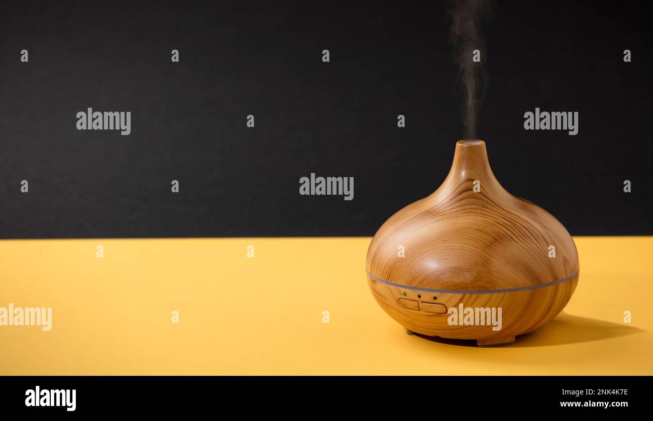deodorante per ambienti in legno con vapore di essenze naturali ad olio, tavolo giallo con fondo nero. Foto Stock