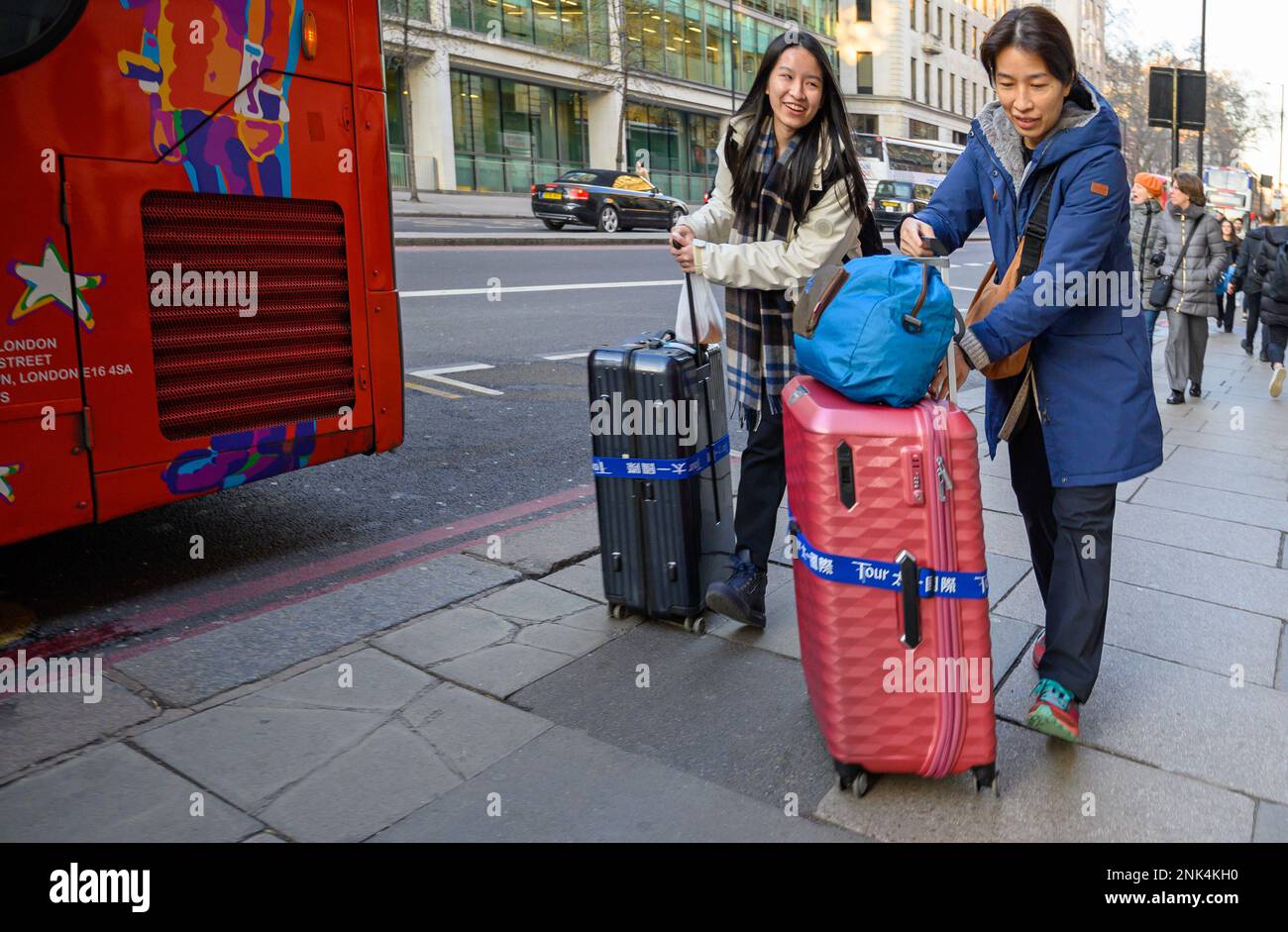 Londra, Inghilterra, Regno Unito. Due donne asiatiche che fanno il peso di un bagaglio pesante nello Strand Foto Stock