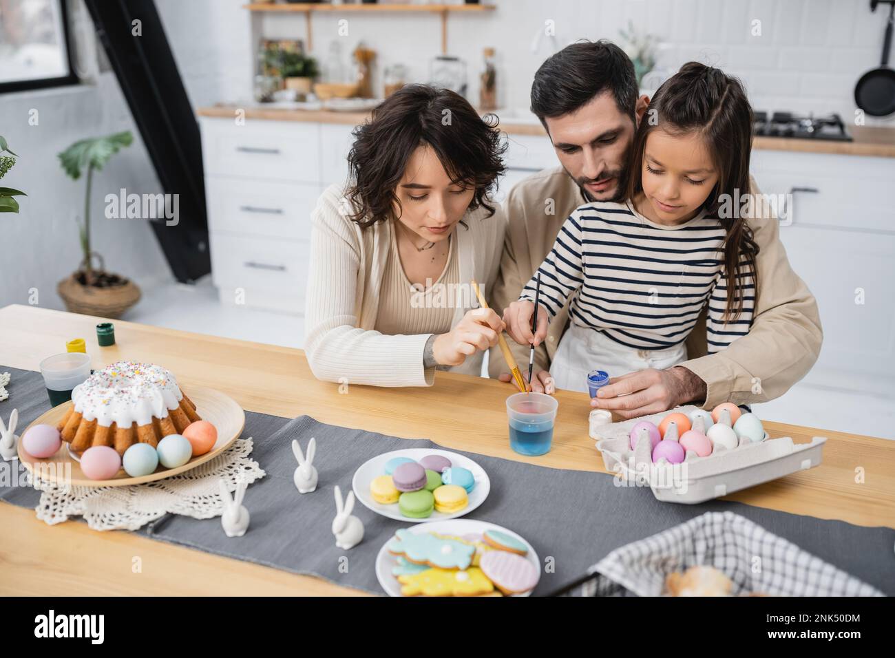 Famiglia colorazione uova di Pasqua vicino torta e biscotti in cucina Foto Stock