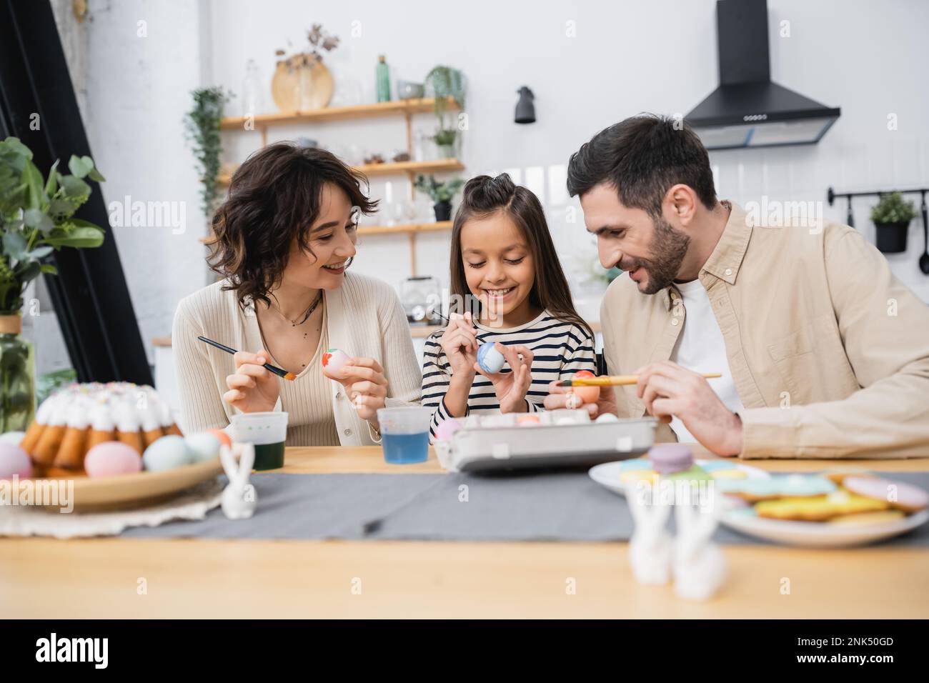 Famiglia colorazione uova vicino torta di Pasqua e arredamento a casa Foto Stock