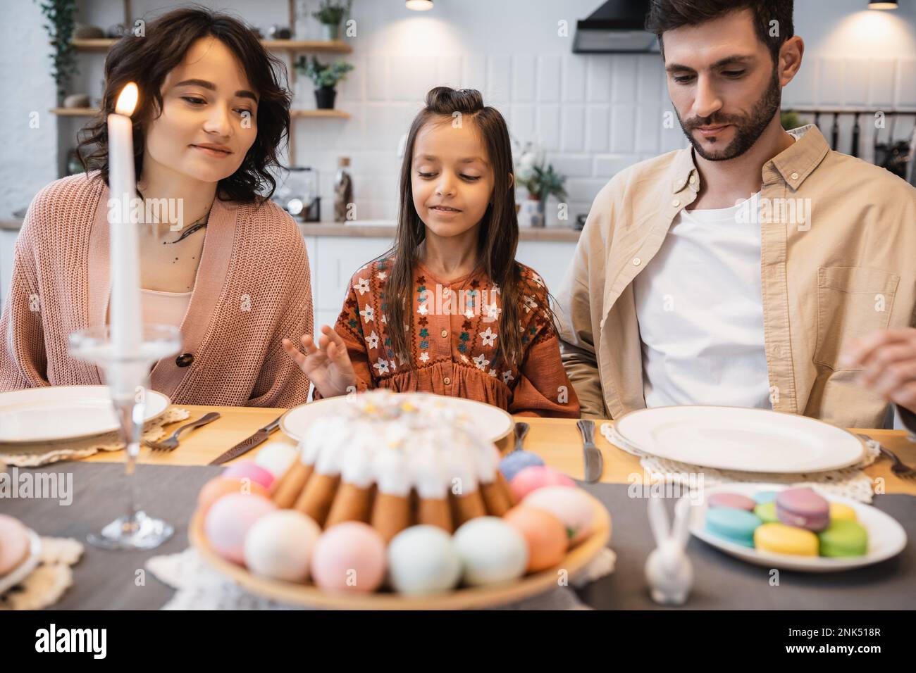 La famiglia si siede vicino alla torta di Pasqua sfocata e candela sul tavolo a casa Foto Stock