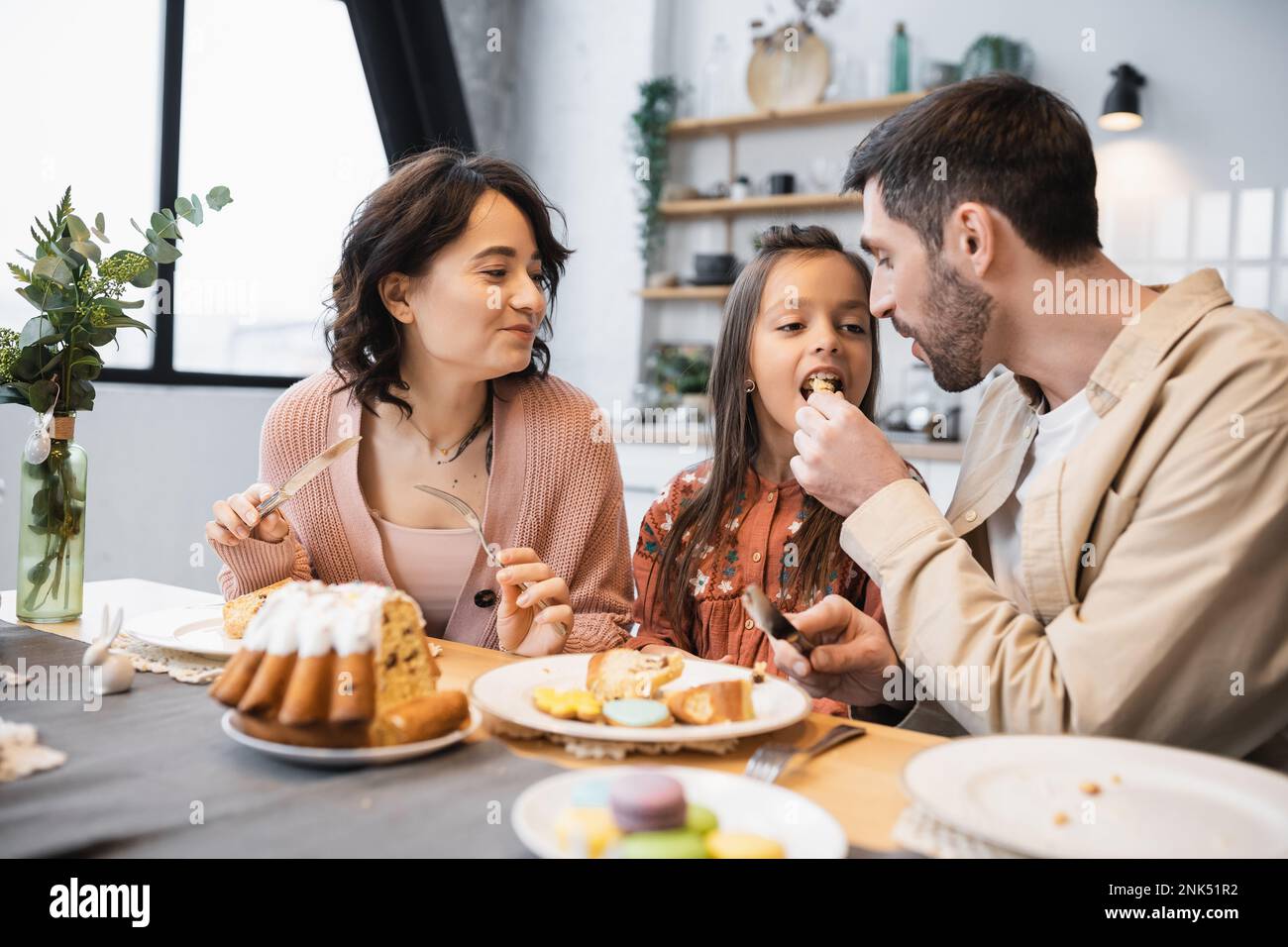 Uomo che nutra la figlia con la torta di Pasqua vicino alla moglie a casa Foto Stock