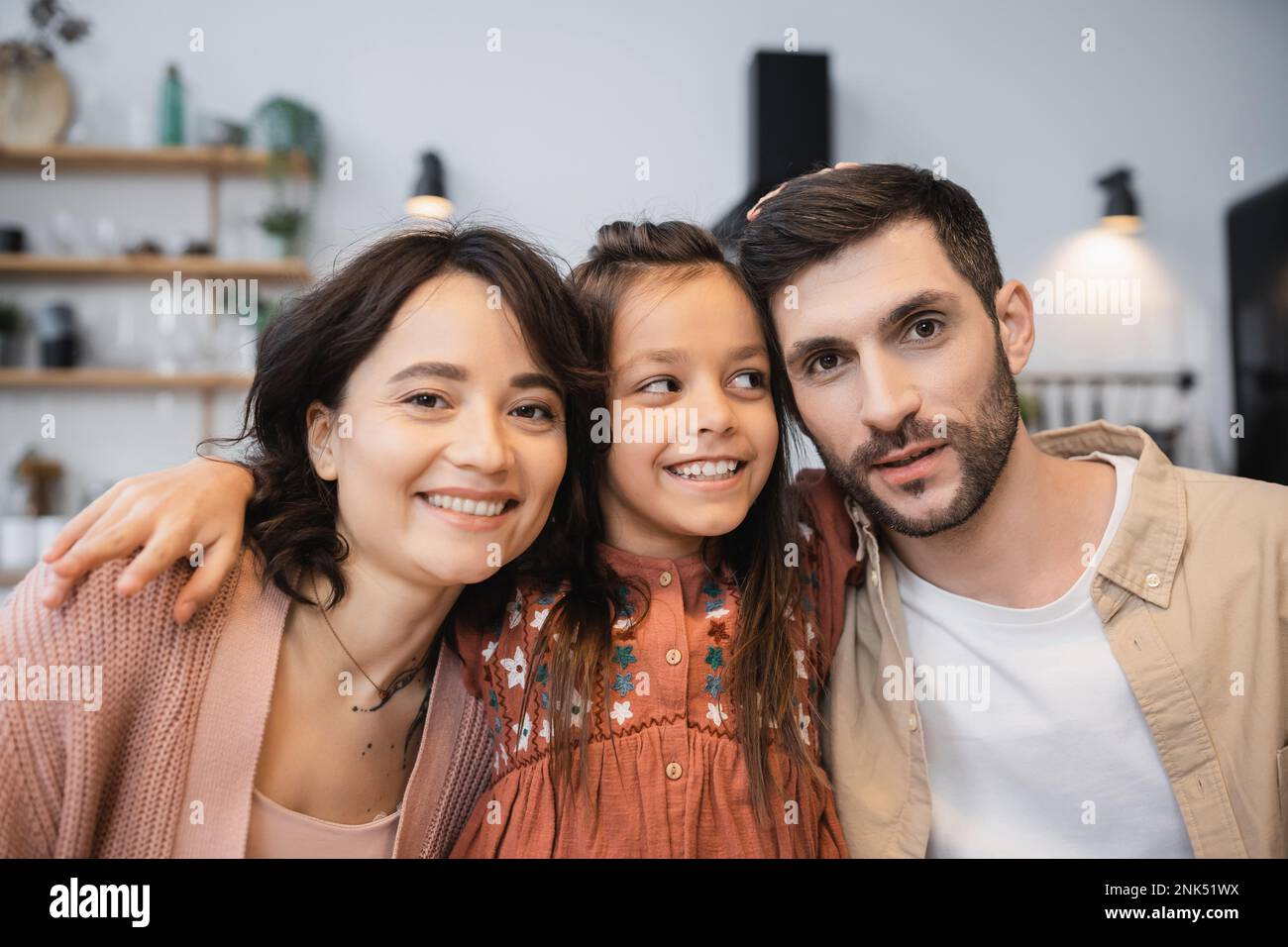 Ragazza sorridente che abbraccia i genitori in cucina a casa Foto Stock