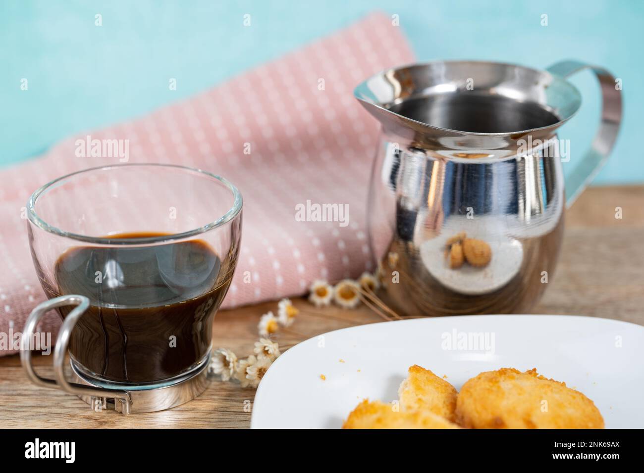 Un piatto di biscotti servito insieme a un espresso con un tovagliolo rosa e fiori secchi Foto Stock