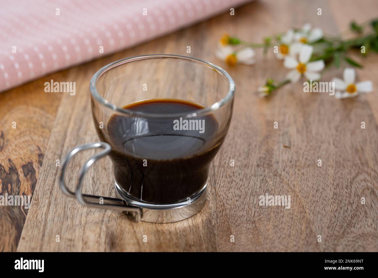 Espresso singolo in un bicchiere su un tavolo di legno con fiori selvatici Foto Stock