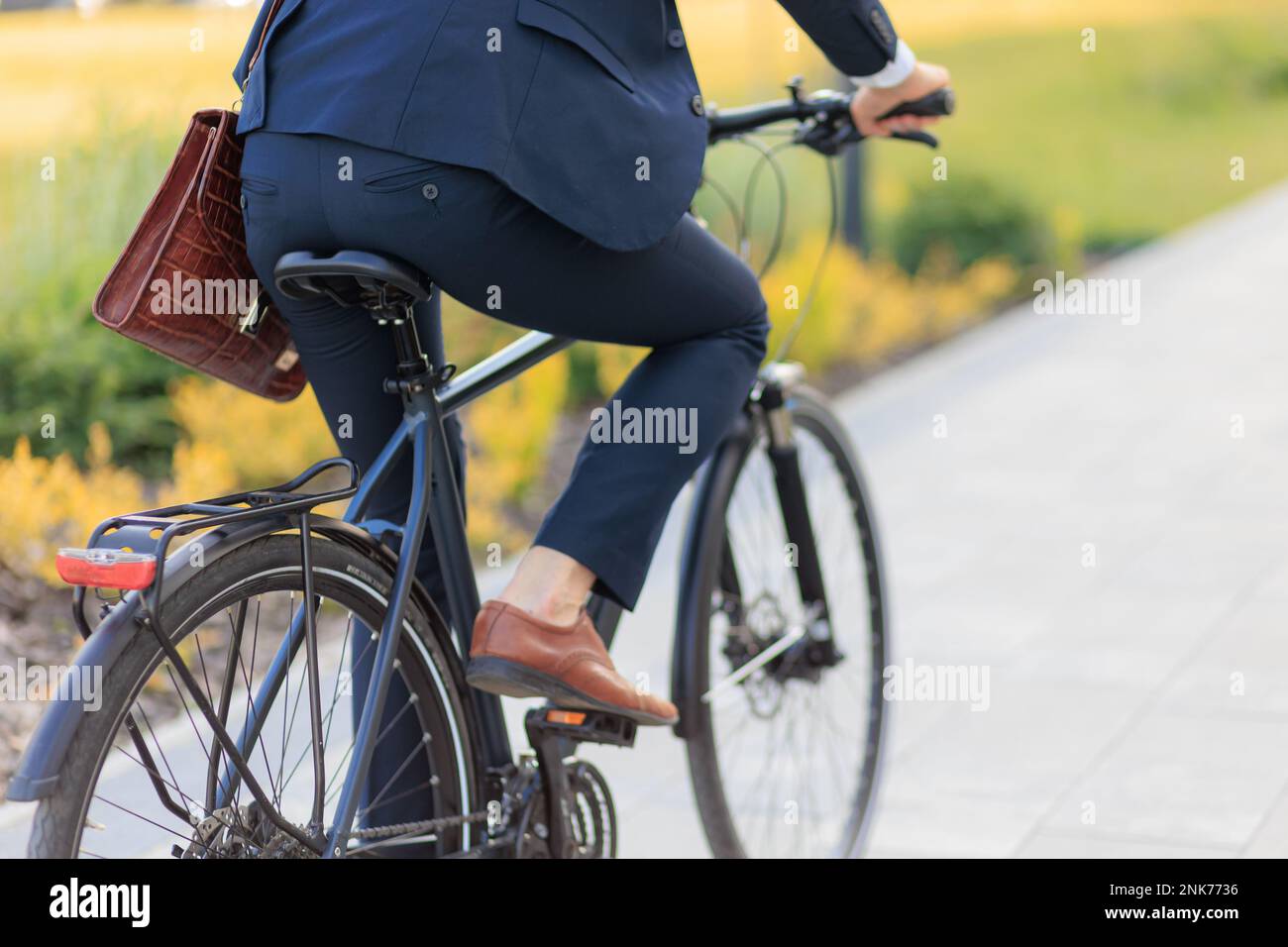 Anonimo imprenditore maschile in bicicletta vestito nero su strada asfaltata di giorno. Vista di raccolto di uomo d'affari in abbigliamento costoso a cavallo in bicicletta in città ar Foto Stock