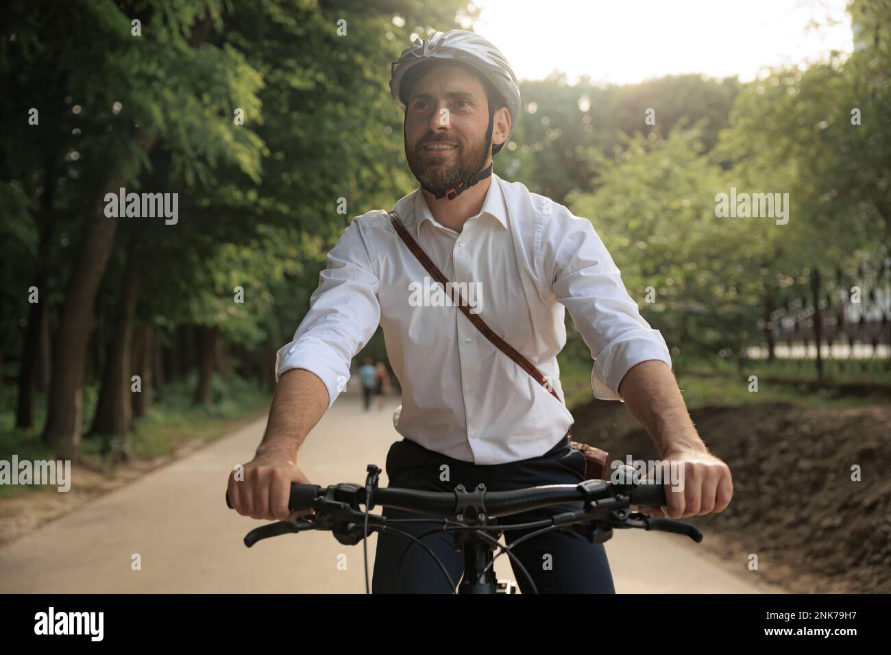 Gioioso imprenditore maschile in casco, in bicicletta lungo il vicolo del parco per lavorare al mattino. Ritratto di lavoratore in casual intelligente guardando avanti, mentre commut Foto Stock