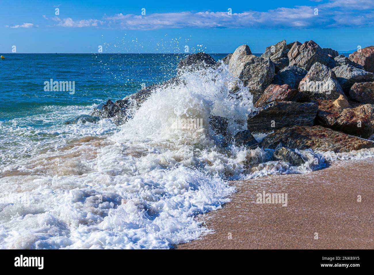 Onde di mare tempestose che colpiscono le rocce su una spiaggia di sabbia sulla Costa Brava, Catalogna, Spagna. Foto Stock